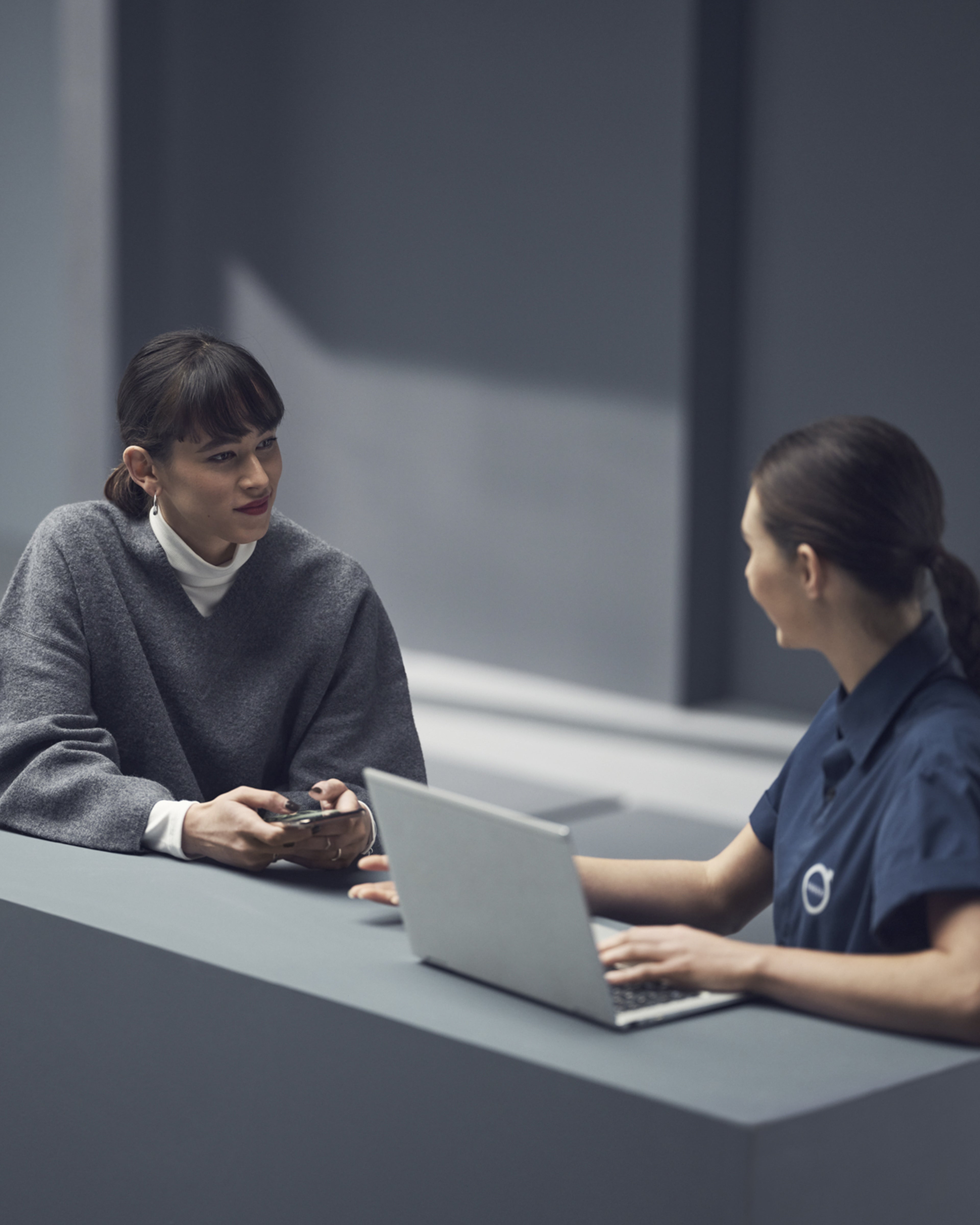 Una encargada de servicio técnico Volvo frente a una computadora atendiendo a una mujer.