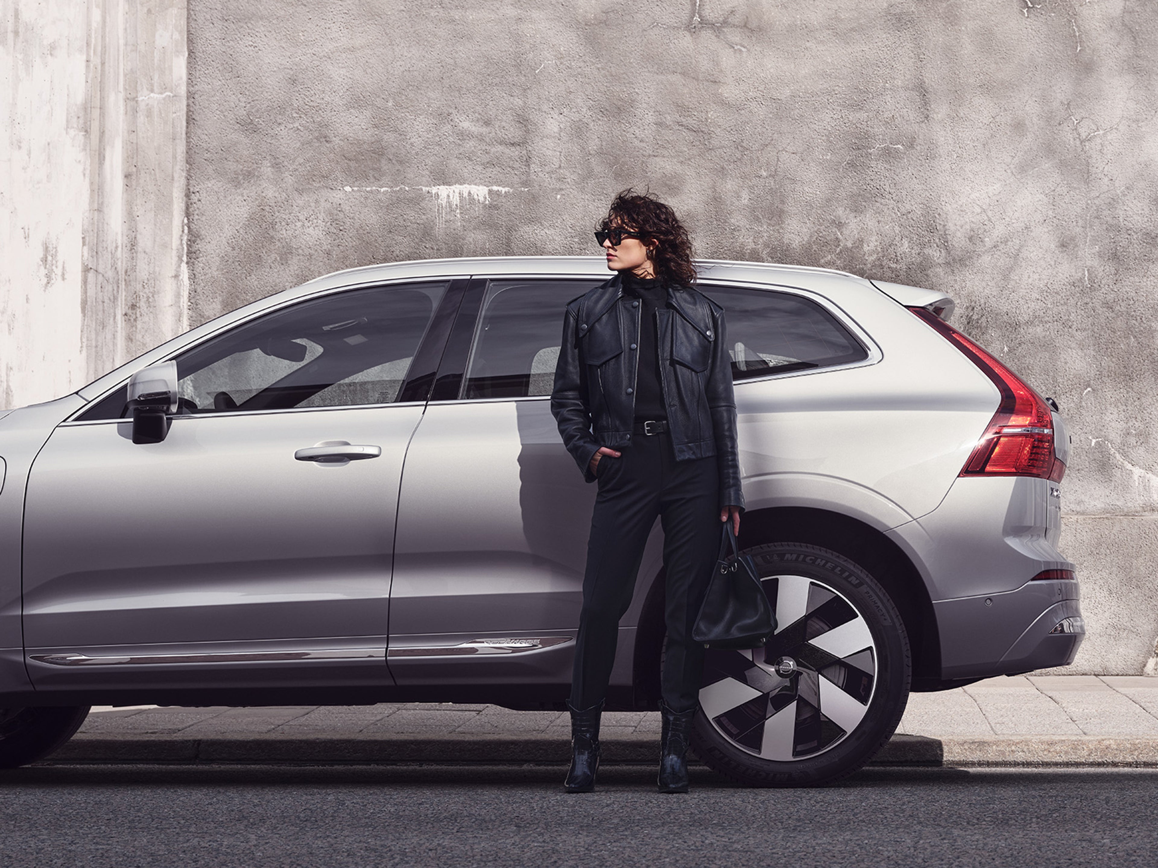 Eine Frau in schwarzer Lederjacke steht vor einem silbernen Volvo XC60.
