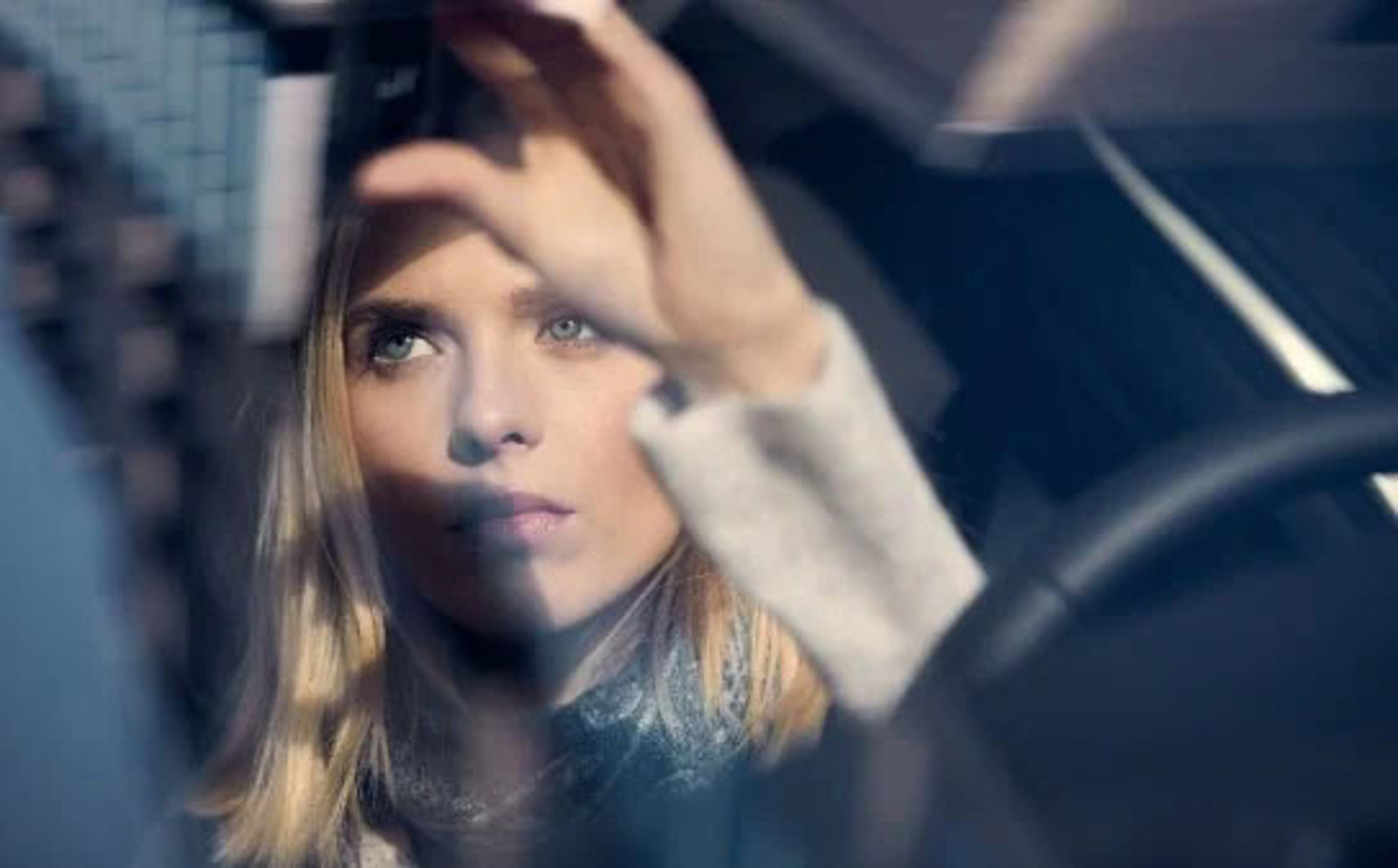 Žena sjedi za volanom automobila i podešava retrovizor.