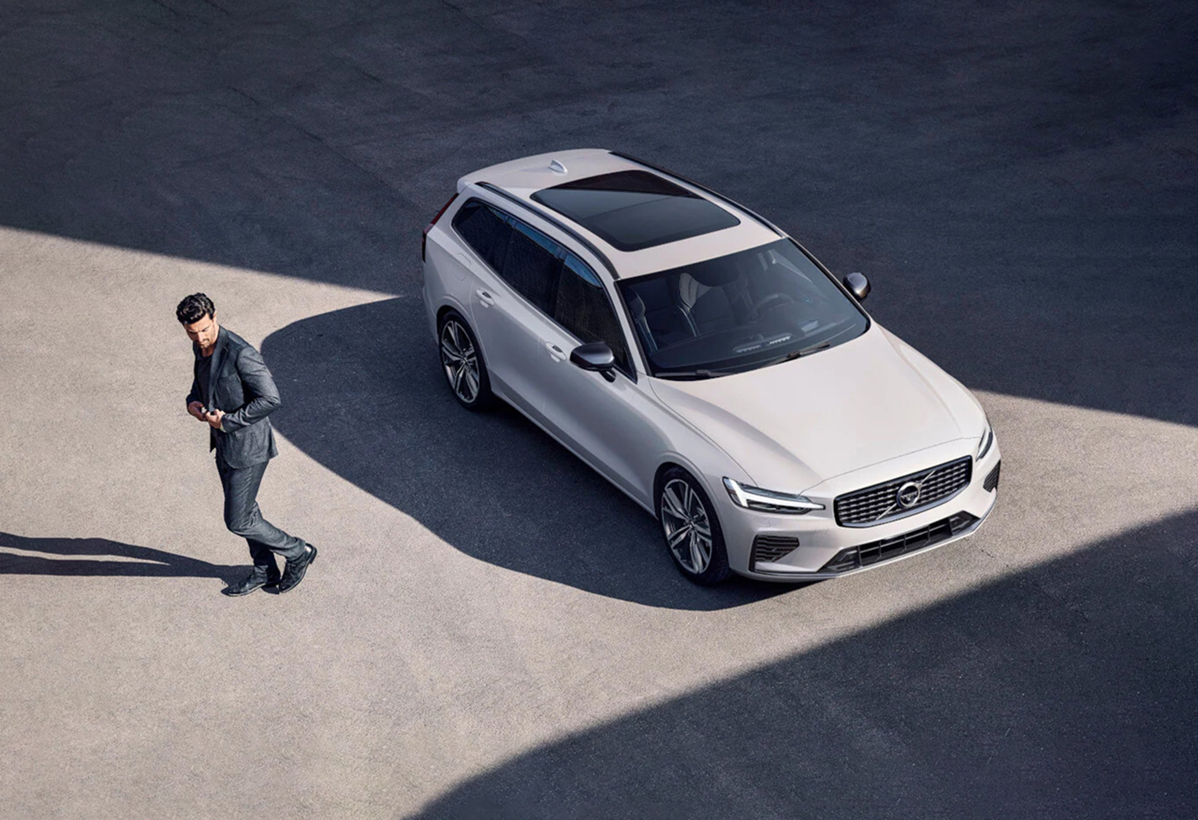 Ein dunkelhaariger Mann im grauen Anzug entfernt sich von einem parkenden Volvo XC60.