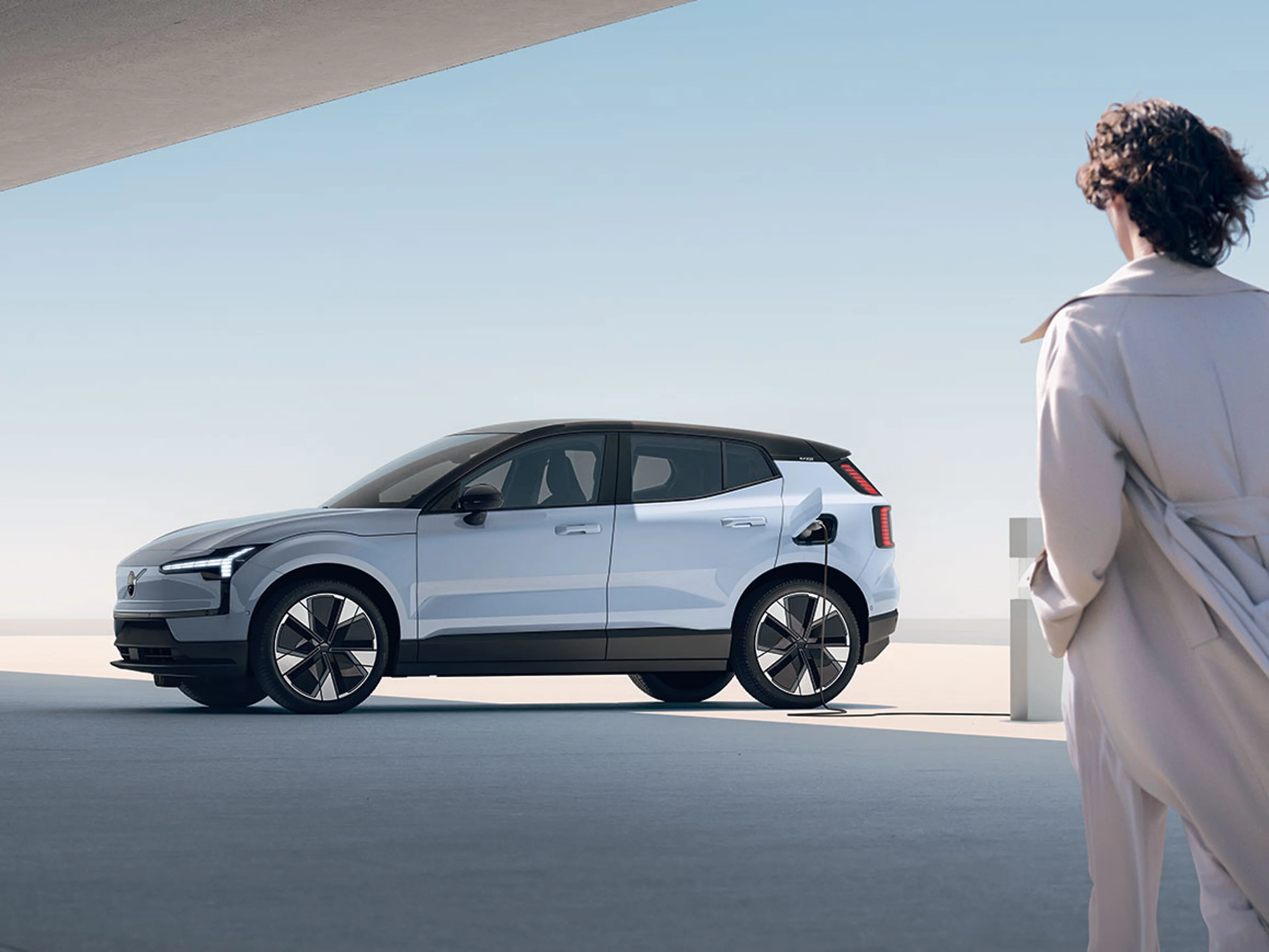 Volvo EX30 en charge, observé par une personne en manteau beige.