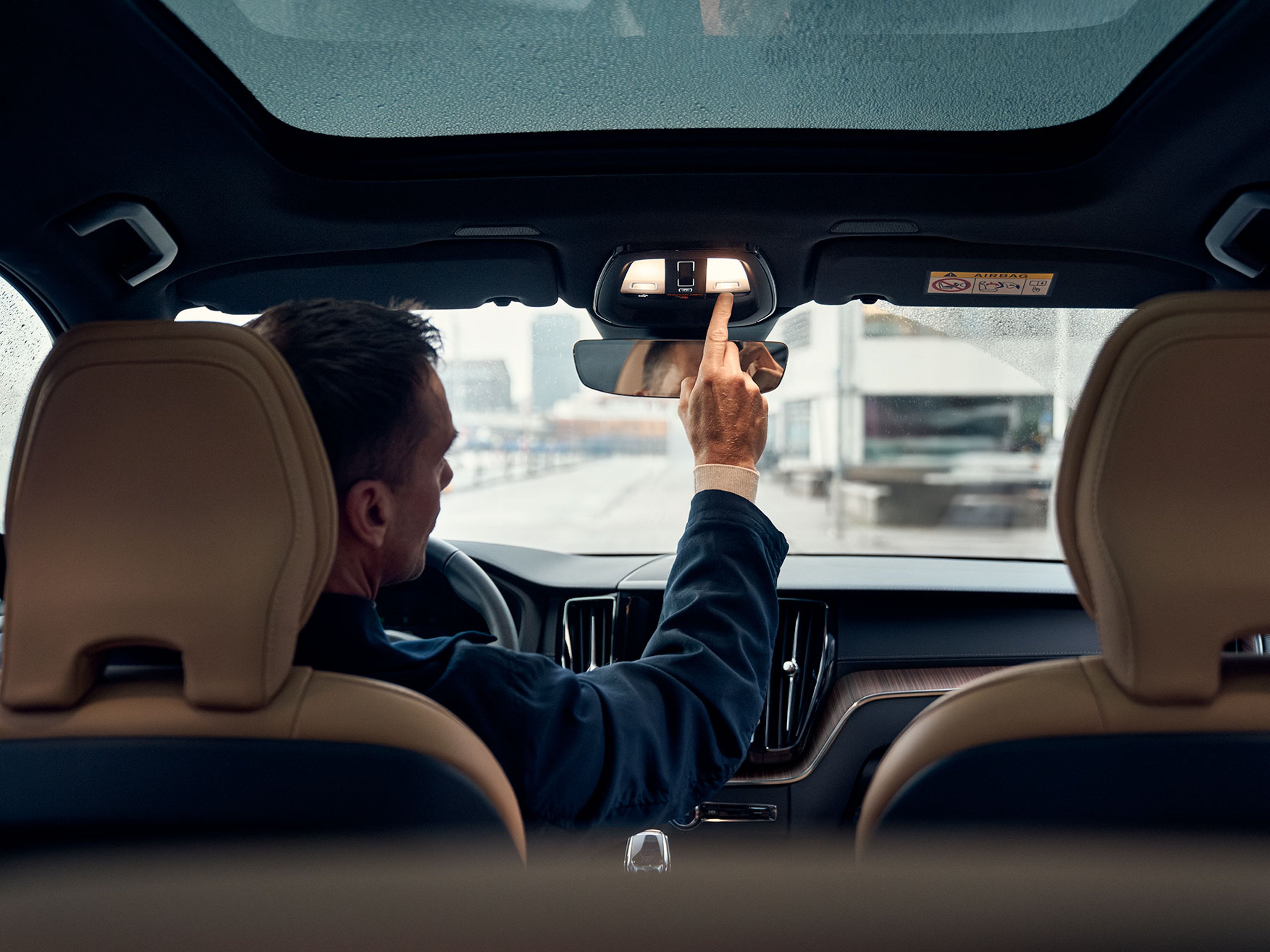 En mand trykker på konsollen i bilens fra Volvos tag for at kontakte vejhjælp, set fra midten af bagsædet.