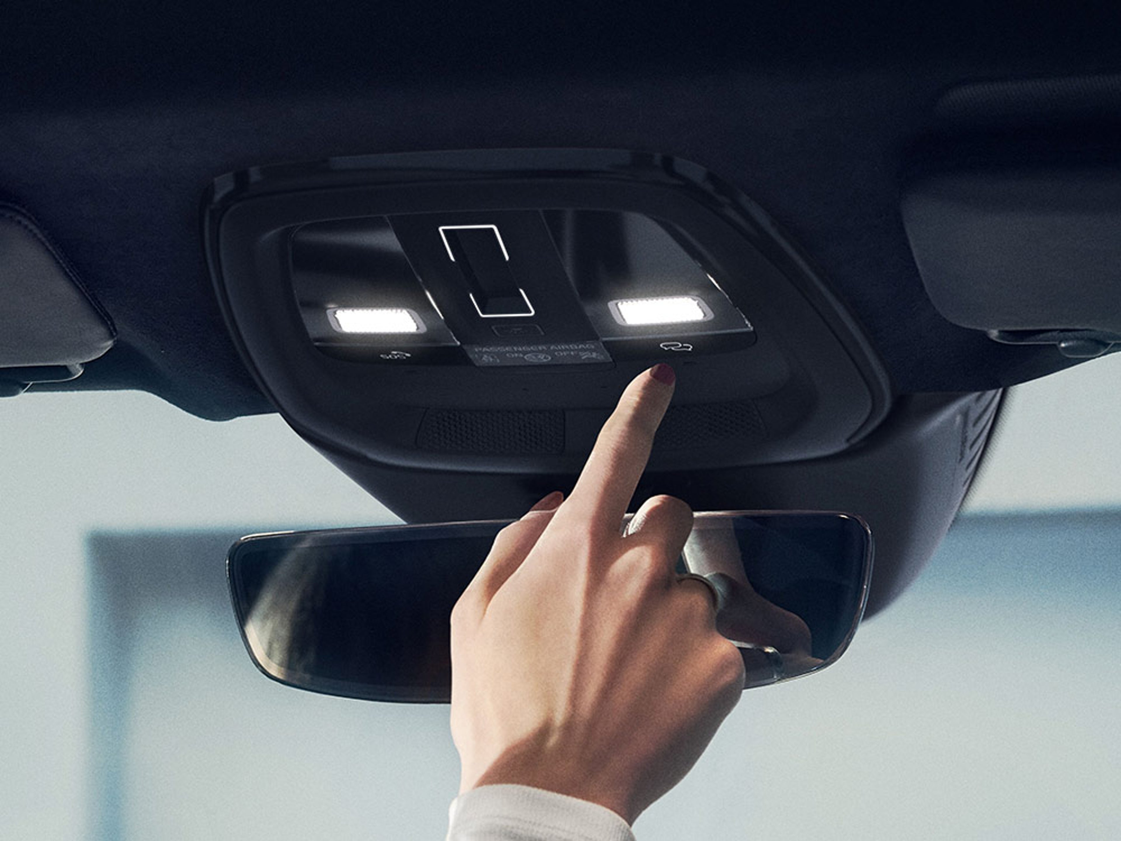 Une main appuie sur le bouton d'assistance sur la console de plafond d'une Volvo.