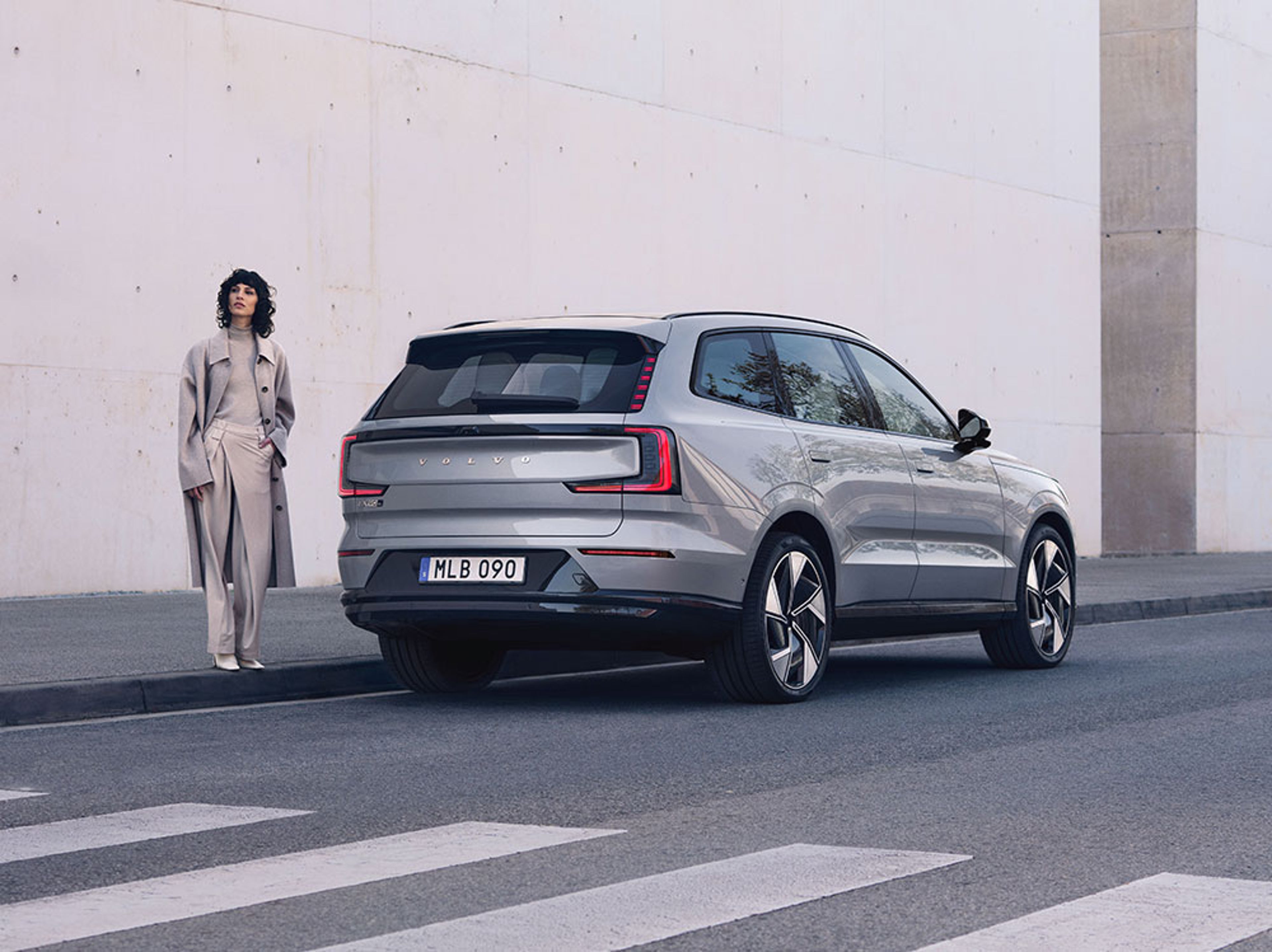 EX90 Gris Brume vu de l’arrière garé près d’un passage piéton avec une femme à son côté