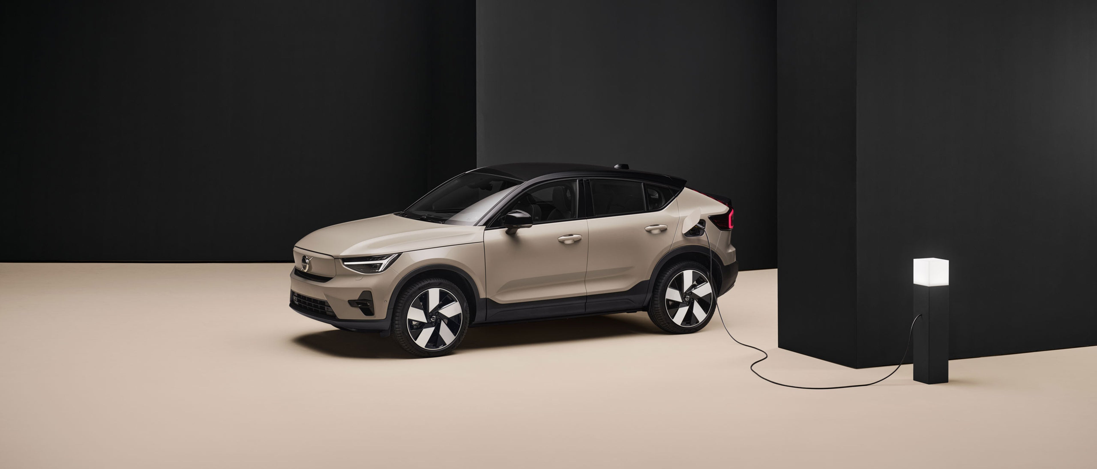 Volvo EC40 beige branché à une borne de recharge dans une pièce minimaliste noire et beige