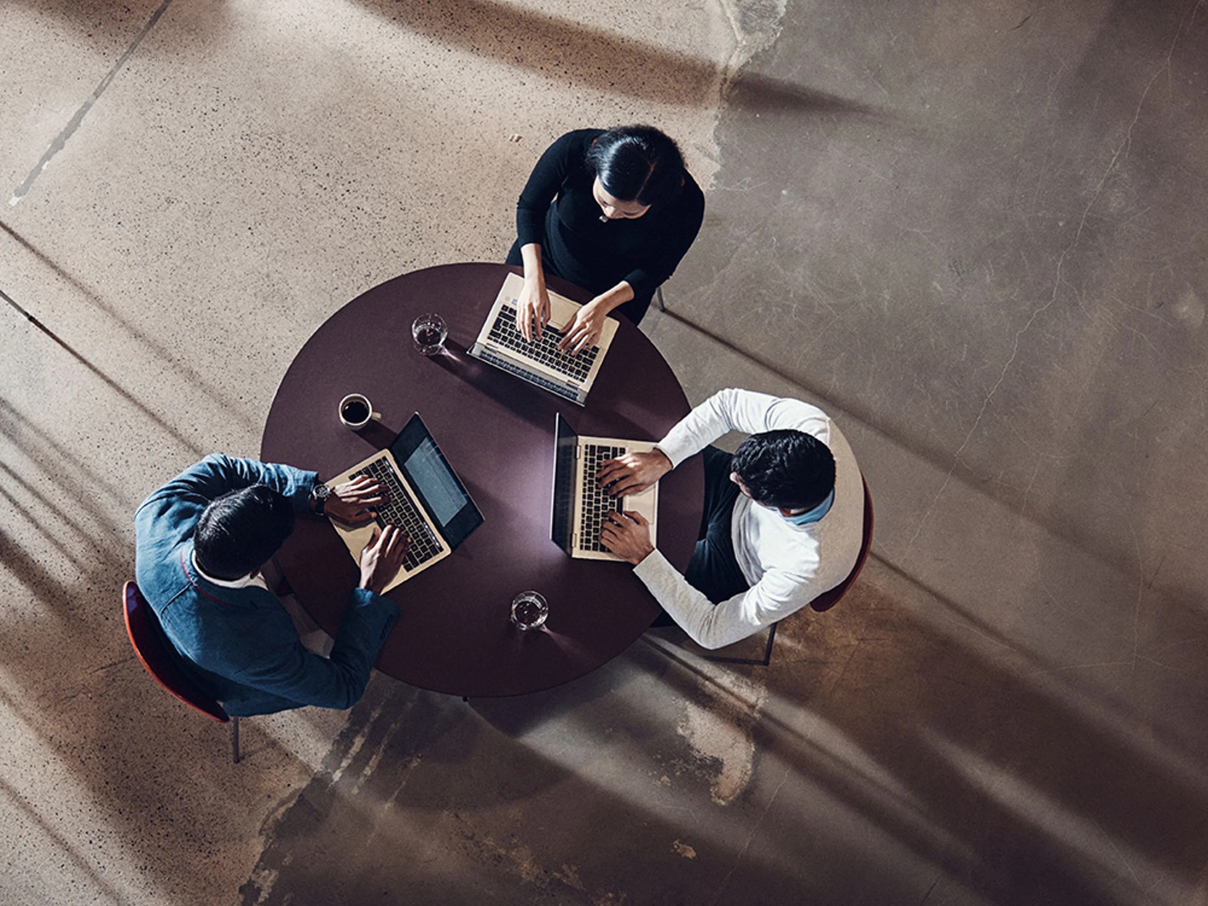 Trois personnes assises autour d'une table, travaillant sur des ordinateurs portables.