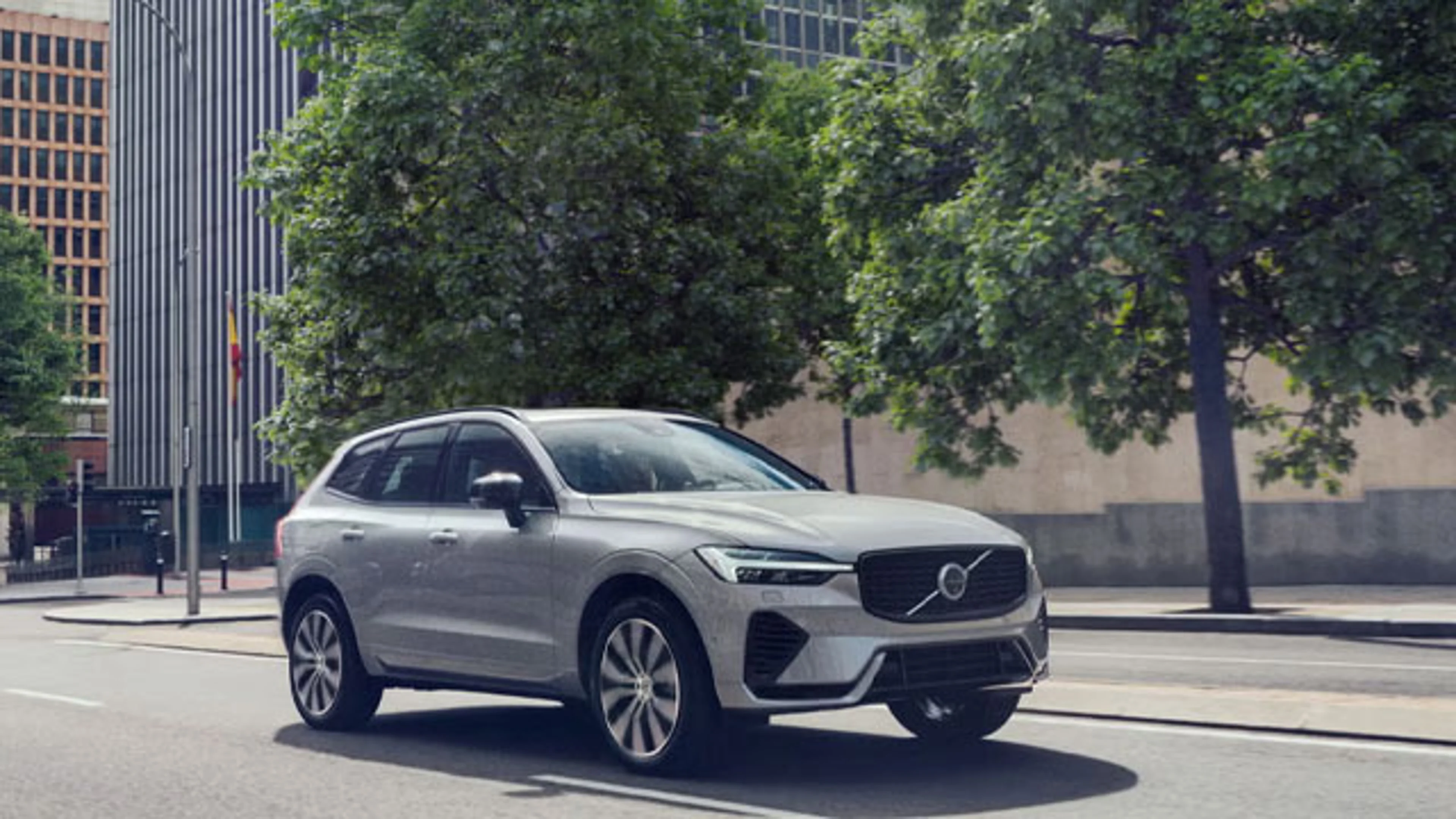Ein silberner Volvo XC60 SUV fährt durch eine Stadt mit Bäumen im Hintergrund.
