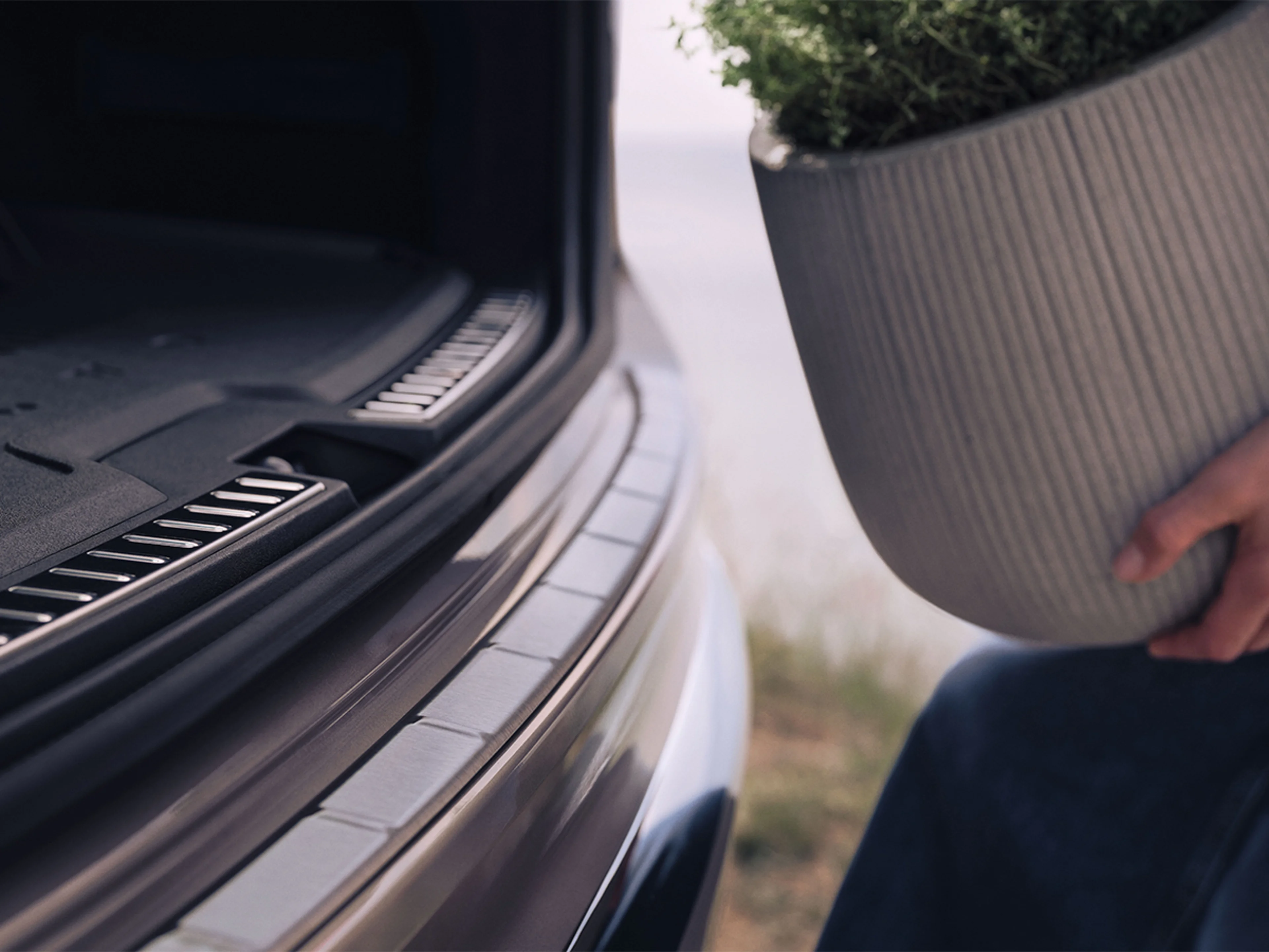 Detaljbild på ett stötfångarskydd på en Volvo XC90 och någon som håller på att lassa in en stor kruka i bagaget