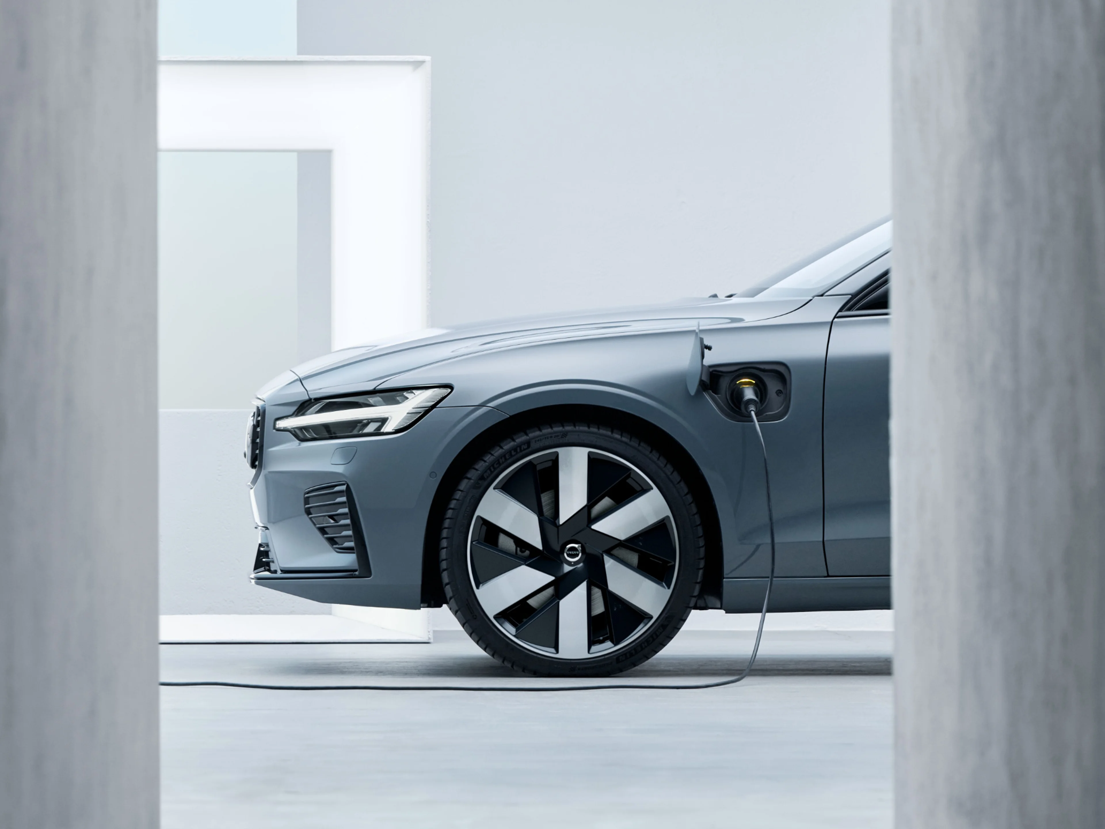 Ausschnitt des vorderen Teils eines blau-grauen Volvo Modells, welches an einem Ladekabel angeschlossen ist.