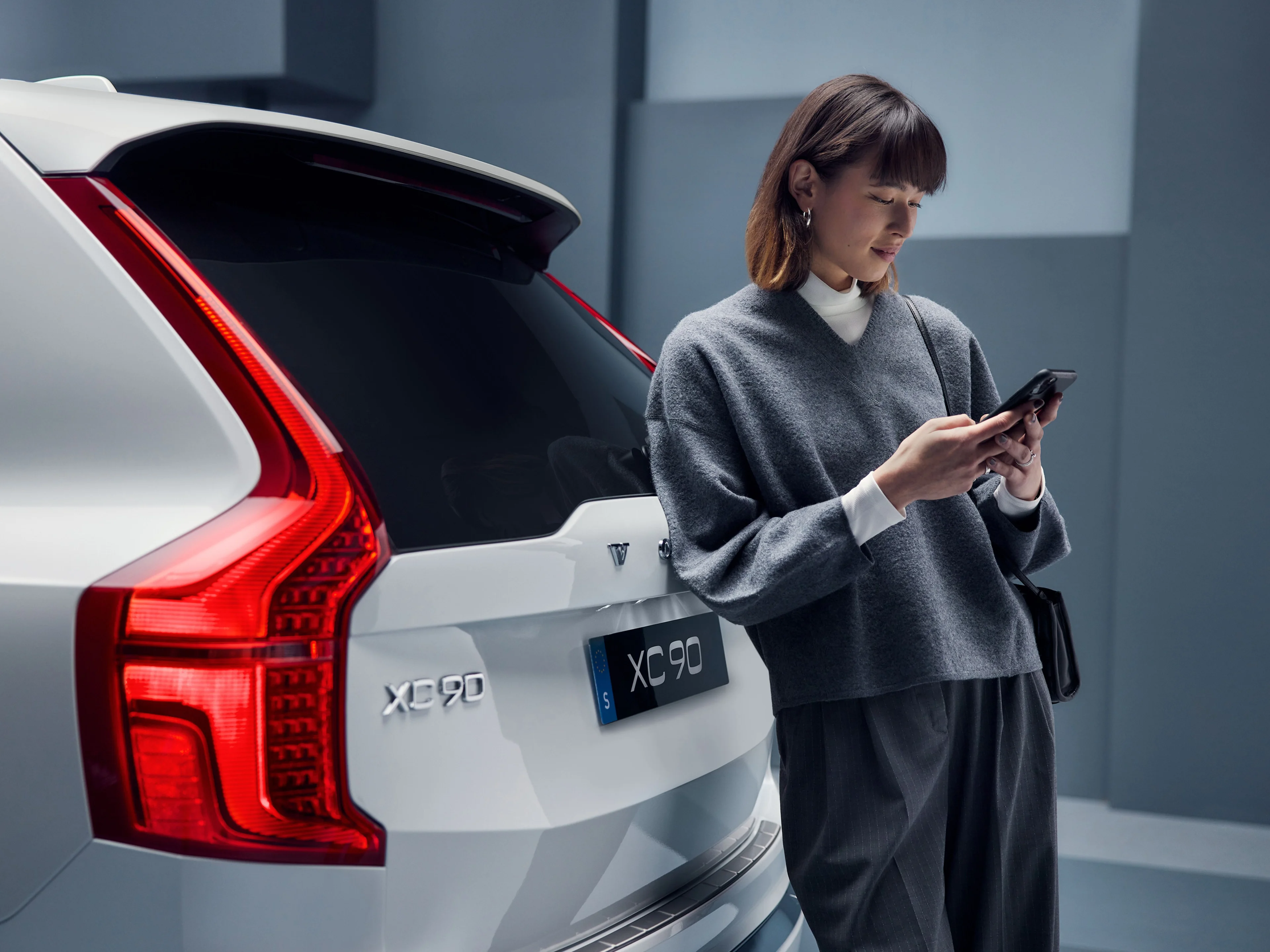 Žena s telefonem v ruce u vozu Volvo XC90