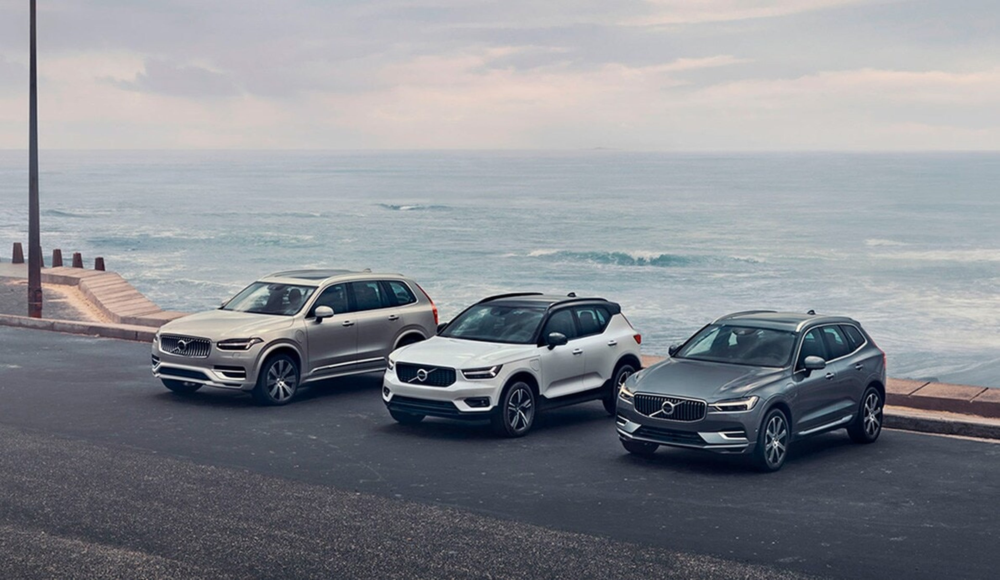 Tre Volvo SUV’er parkeret på en kystvej med havet i baggrunden. Fra venstre mod højre er de sølv, hvid og grå og udstråler elegance og stil.