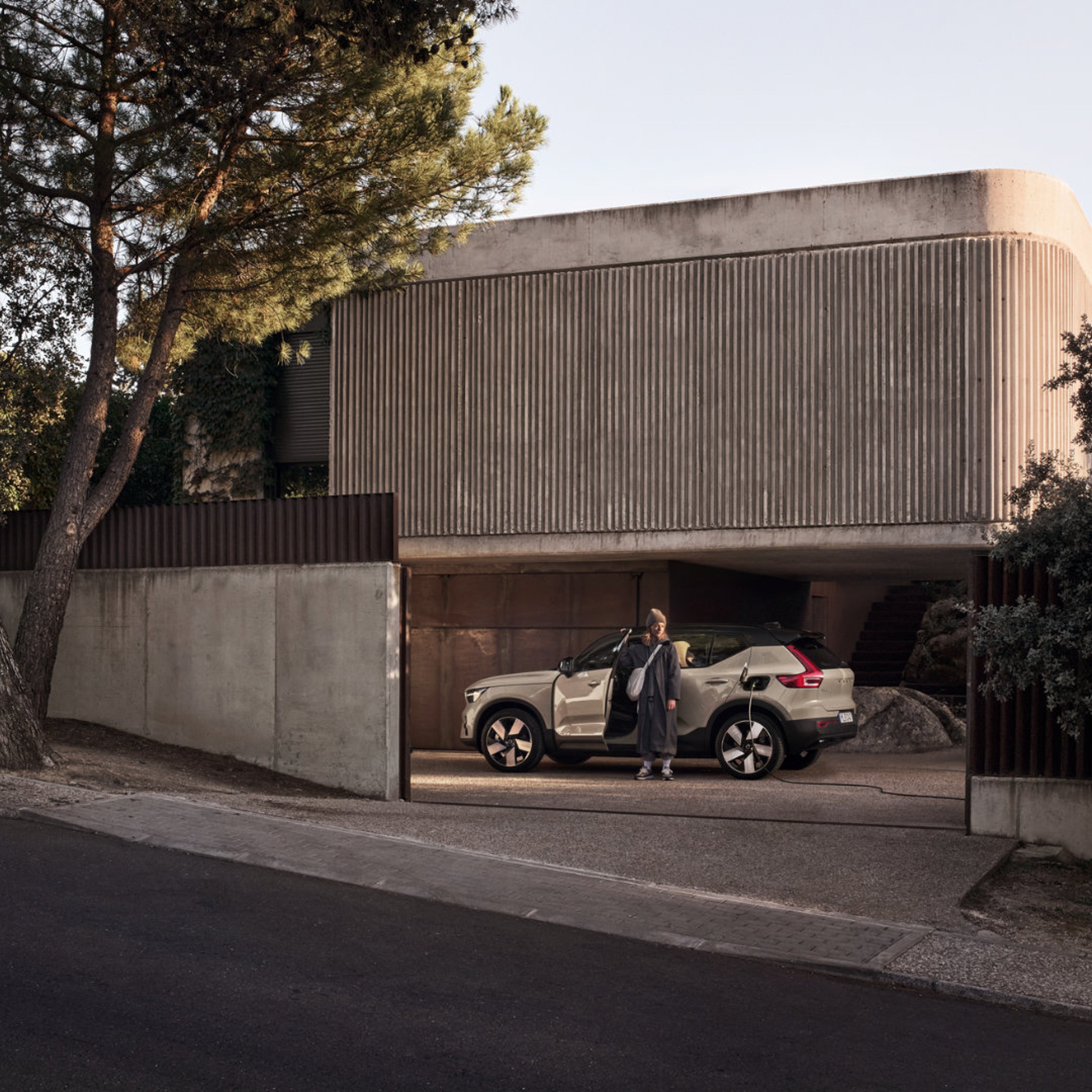 Eine Frau steht an der offenen Tür eines beigen Volvo XC40 SUV, der vor einem Haus steht.