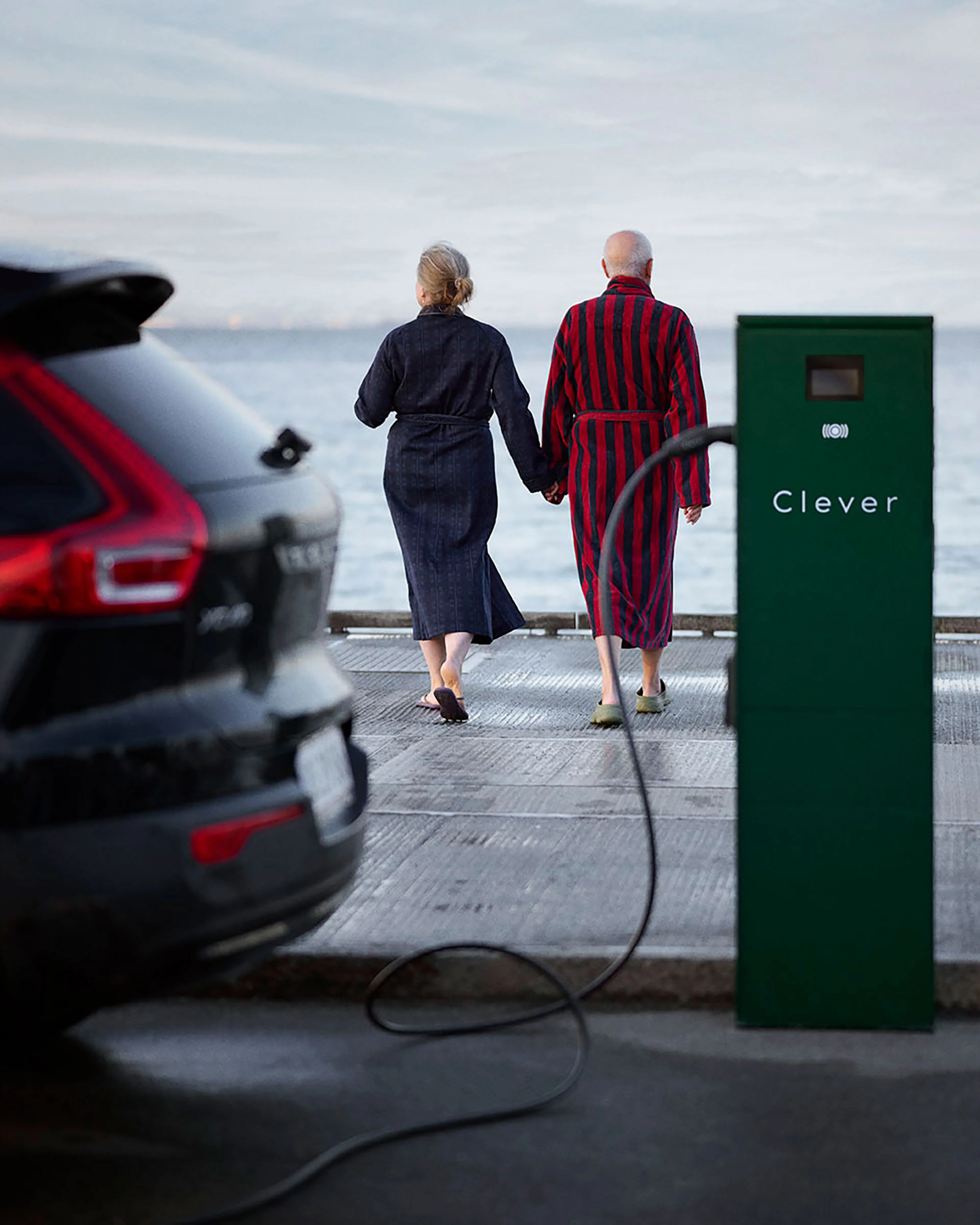 Volvo til opladning ved Clever-station, mens ældre par i badekåber går mod vandet for vinterbadning