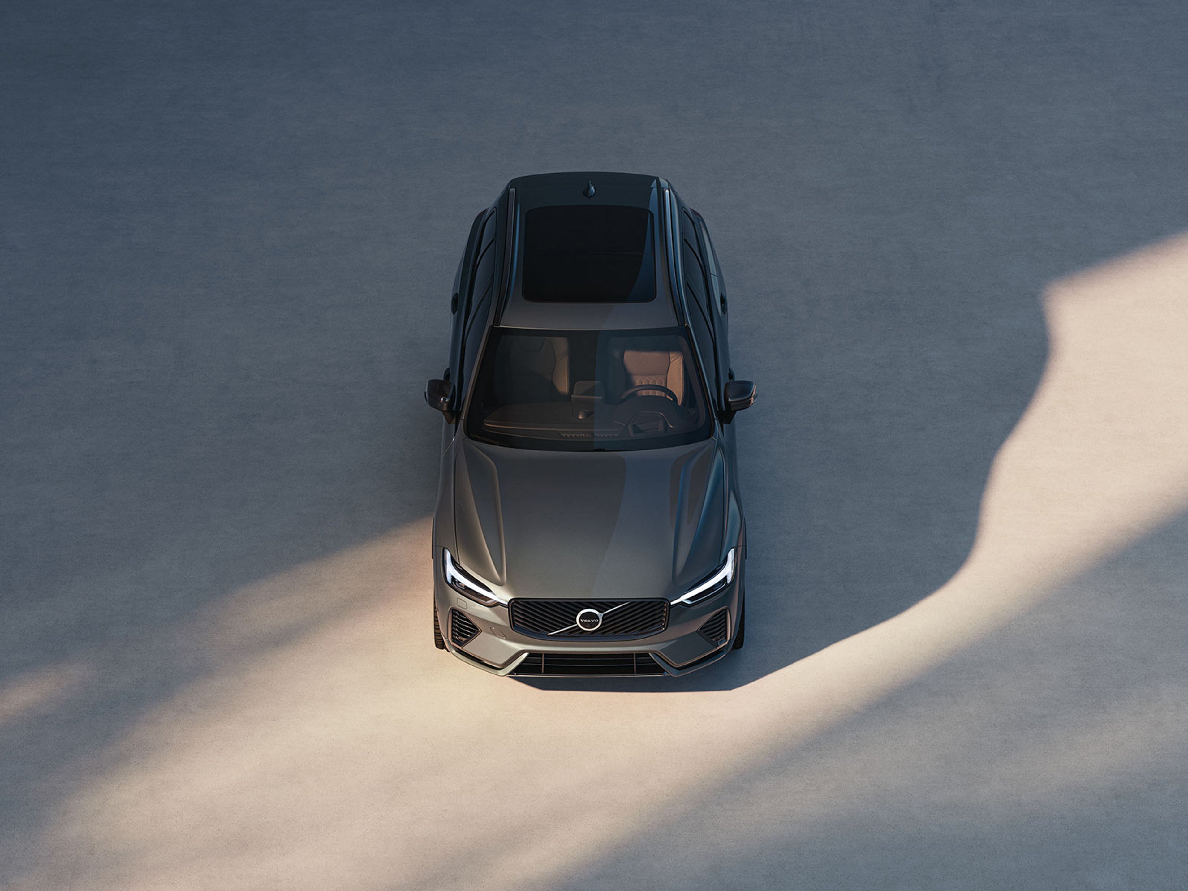 En Volvo XC60 sedd ovanifrån, parkerad på en ljus betongyta med solbelysta och skuggade områden runt bilen.