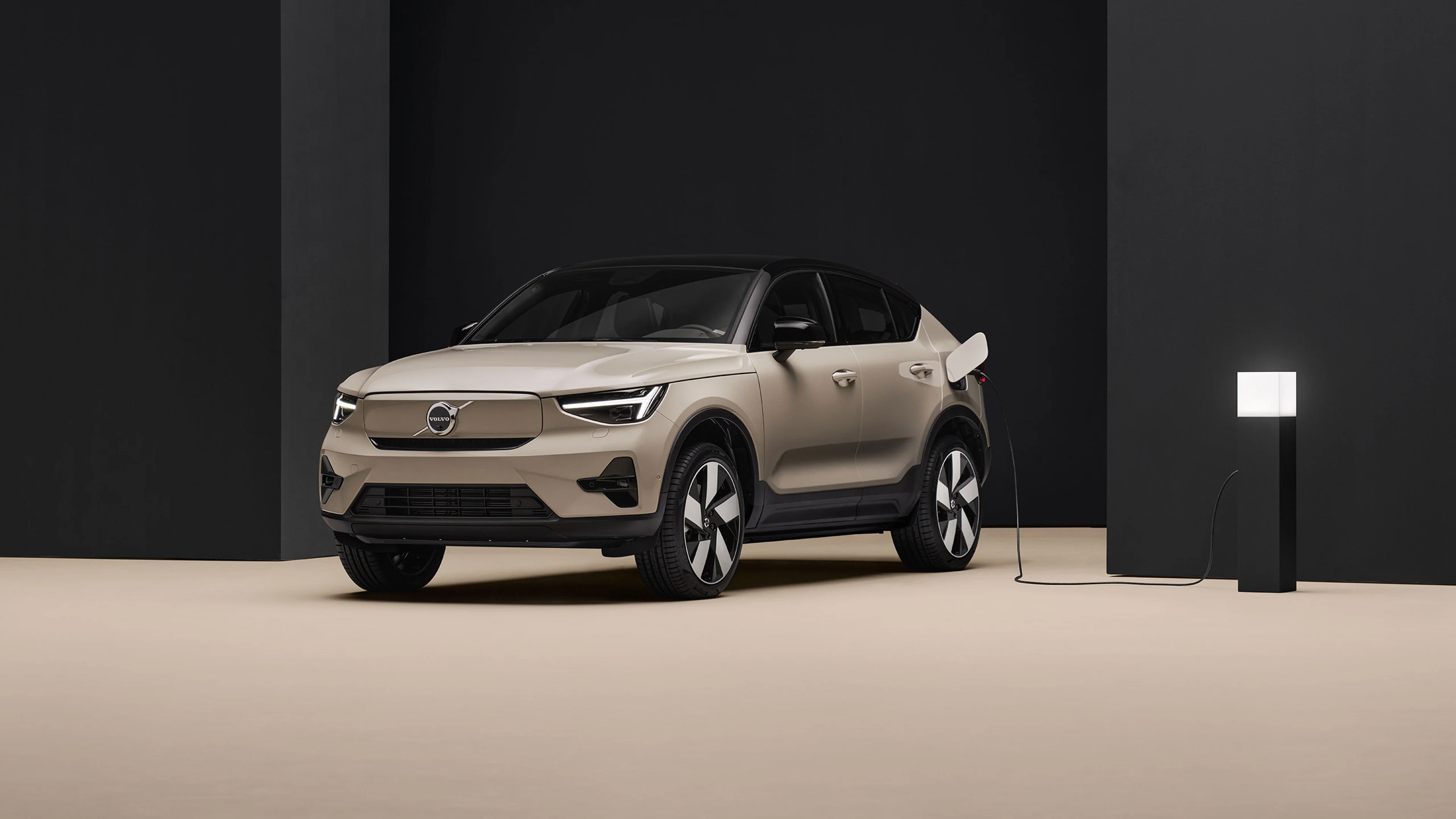 Voiture électrique Volvo EC40 beige en charge, fond minimaliste noir et sol beige