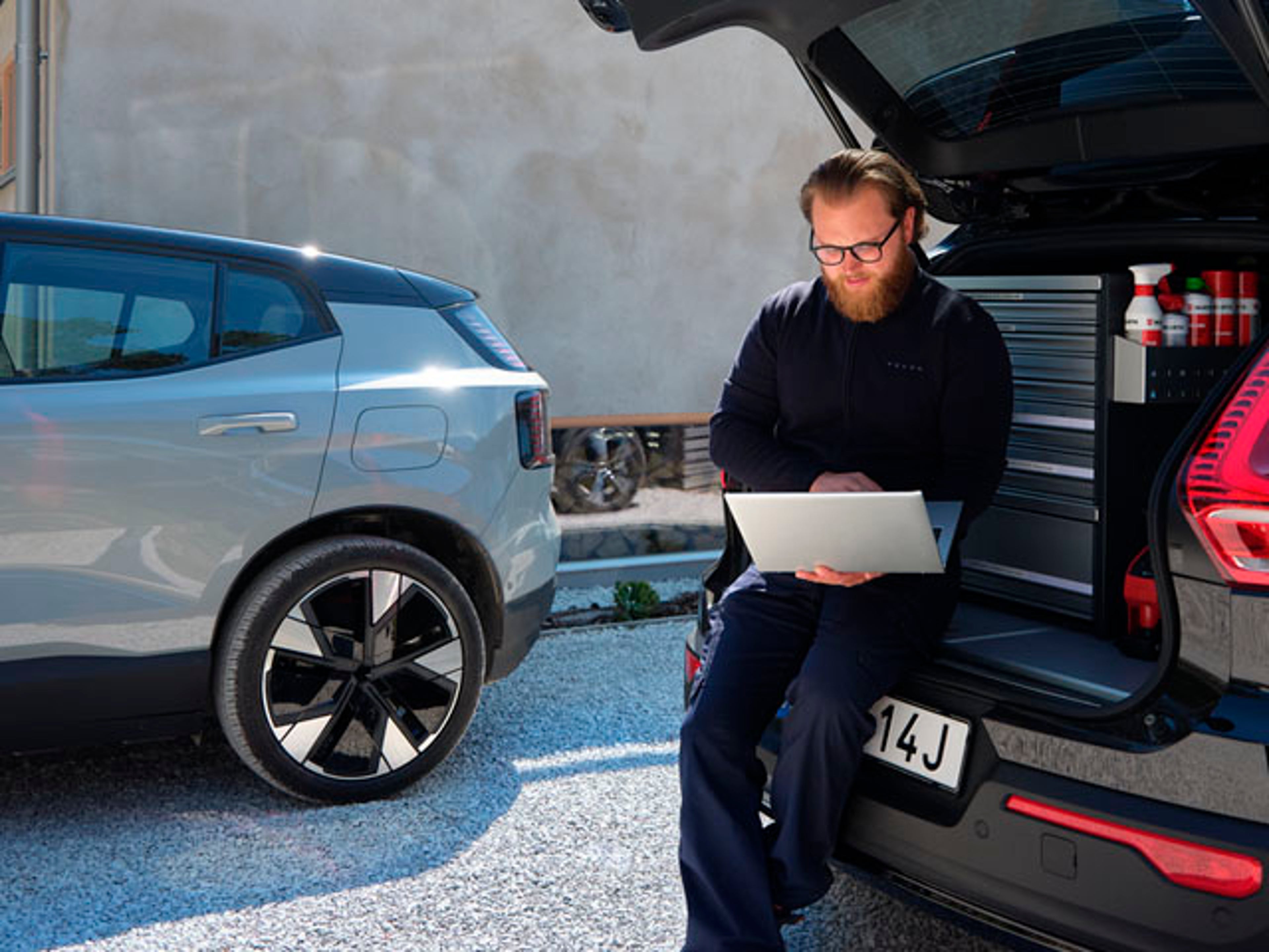 Un hombre con un ordenador y detrás un Volvo EX30 eléctrico