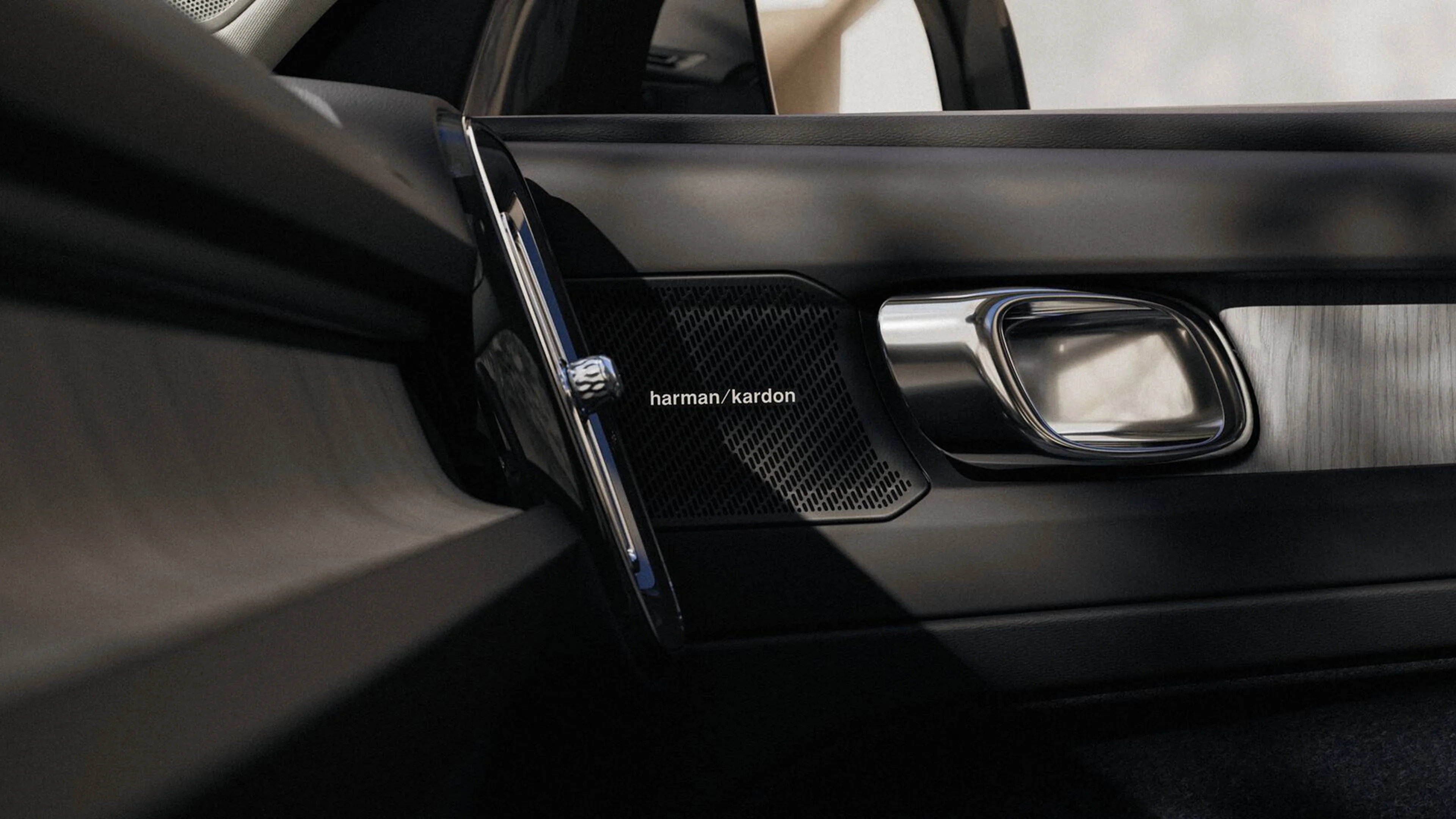 Haut-parleur Harman Kardon dans porte de voiture, poignée chromée et intérieur cuir noir.