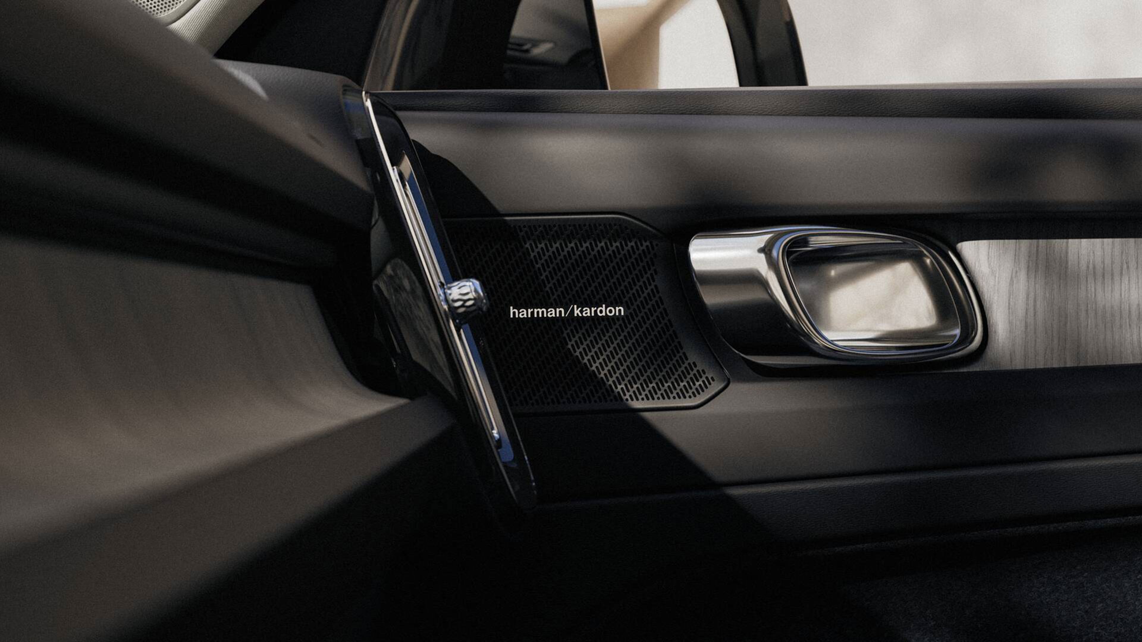 Haut-parleur Harman Kardon dans porte de voiture, poignée chromée et intérieur cuir noir.