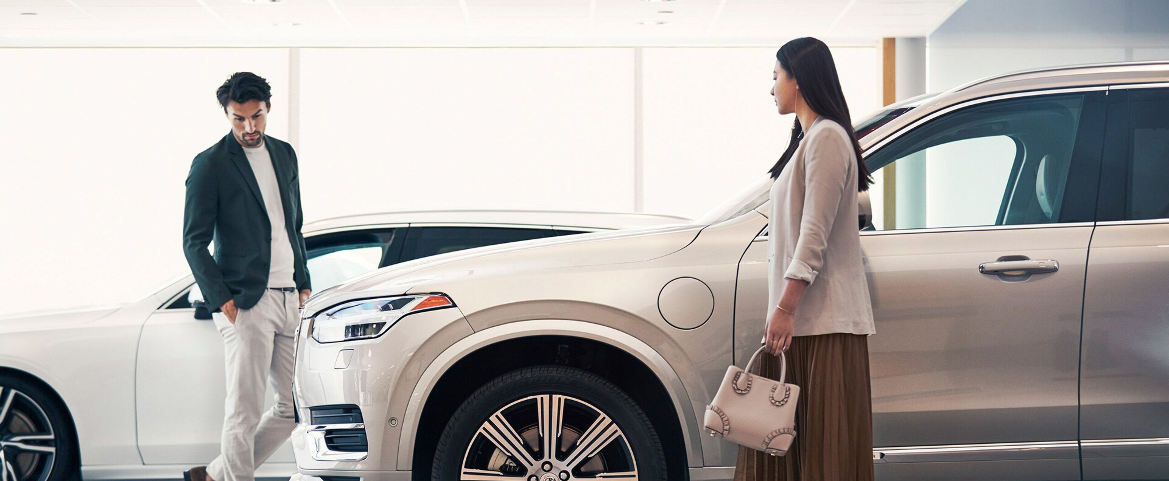 Vedere laterală a modelului Volvo XC90 — clienții examinează mașina din apropiere.