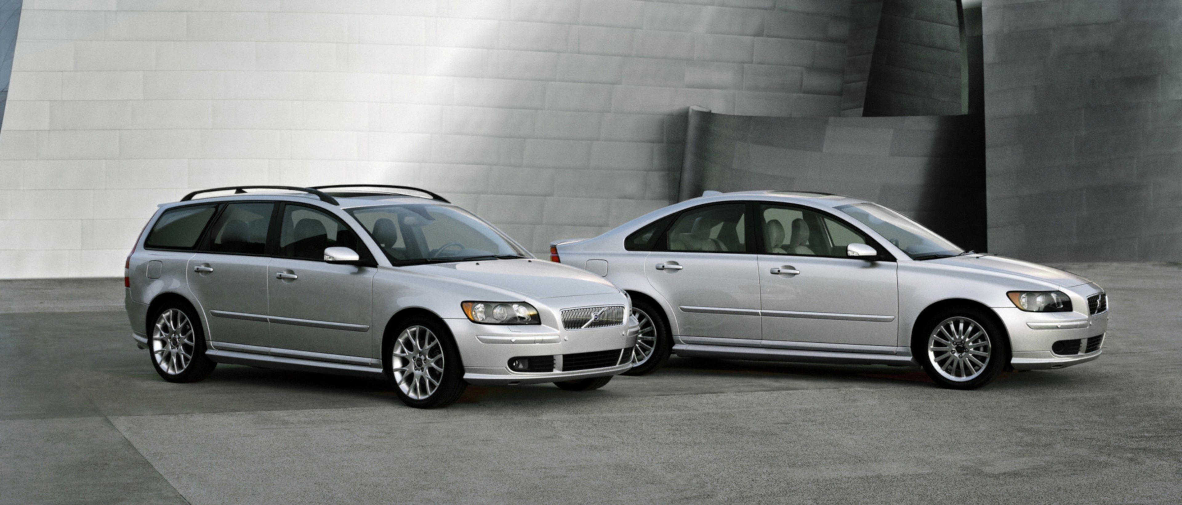 Zwei alte Volvo Modelle stehen nebeneinander vor einem grauen Gebäude