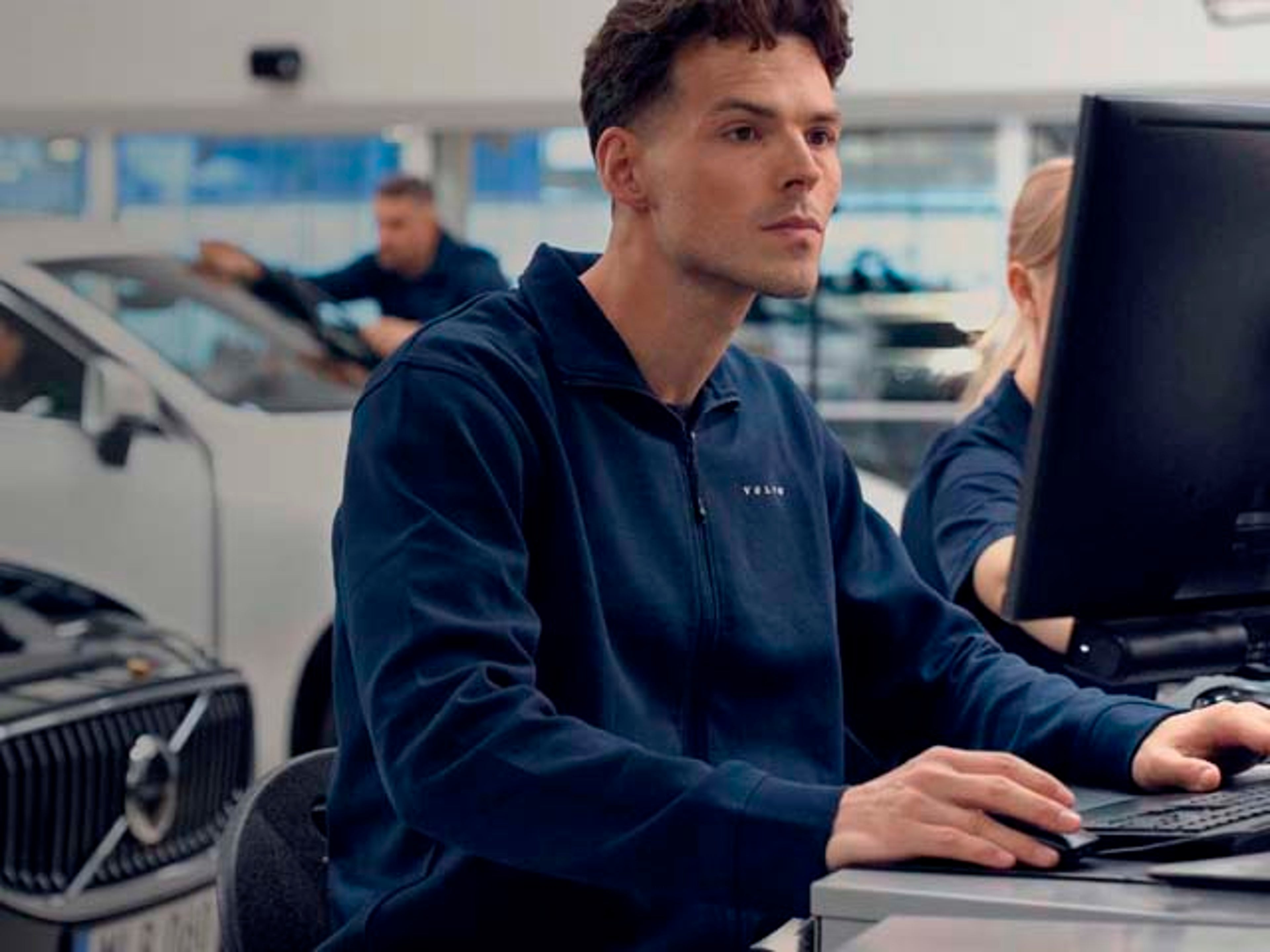 Un técnico en un servicio oficial Volvo comprobando datos en un ordenador y vehículos volvo al fondo