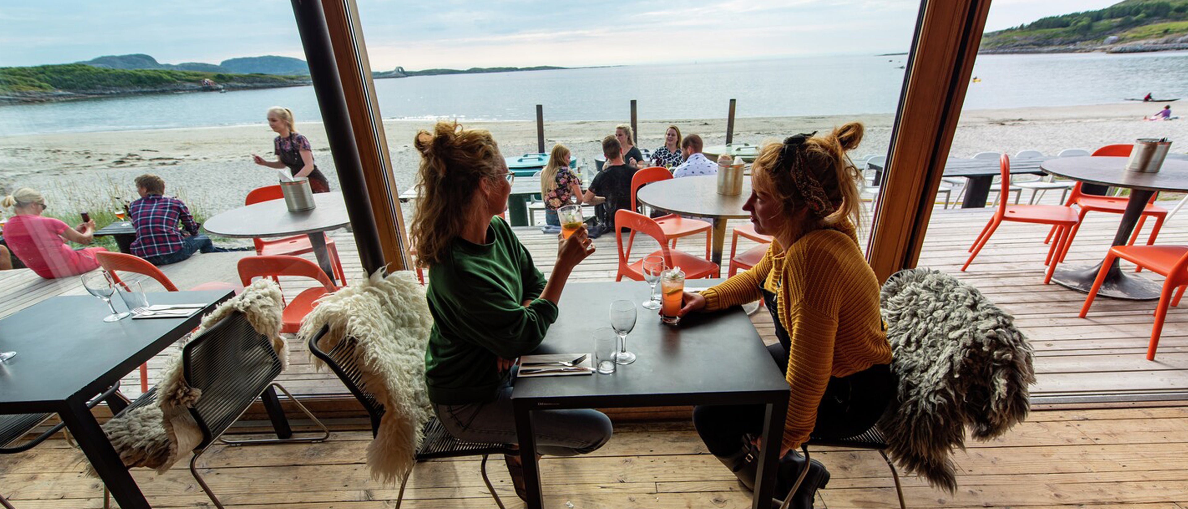 to damer som tar seg noe og drikke på restaurant med utsikt over havet
