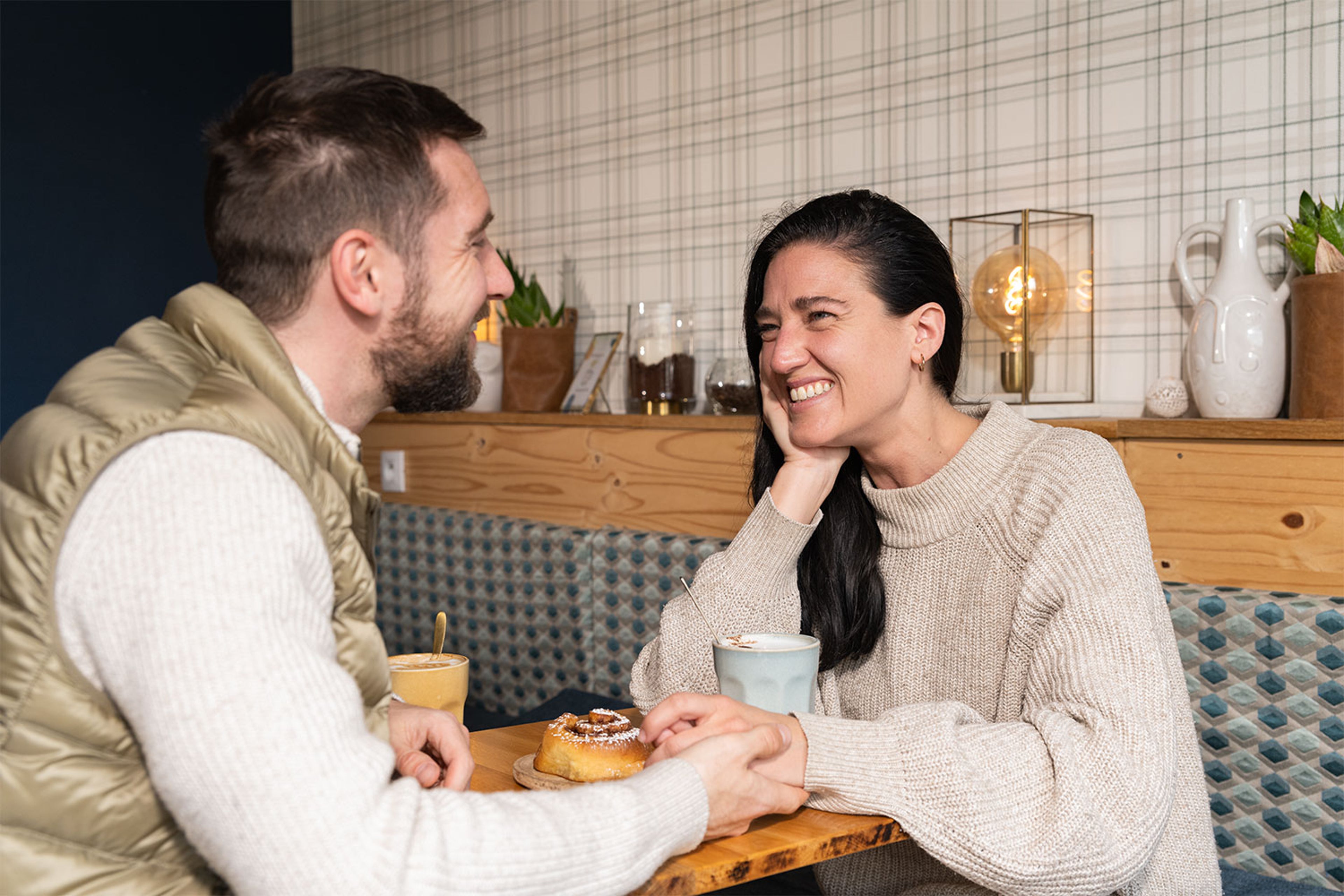 Deux personnes assises à une table de café, se tenant les mains avec boissons chaudes et pâtisseries.