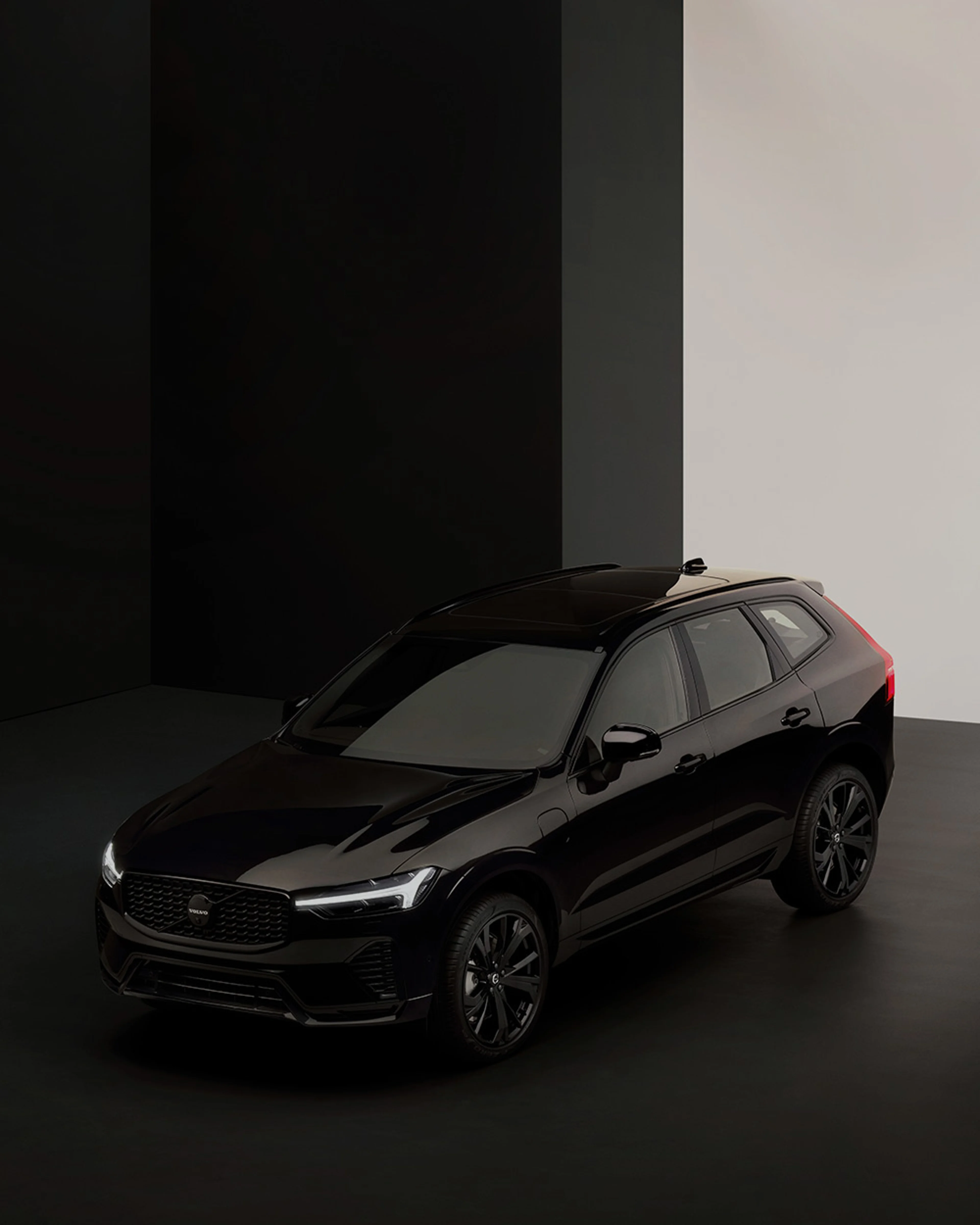 Une voiture noire de type SUV est présentée dans un studio avec un fond noir et blanc contrasté.