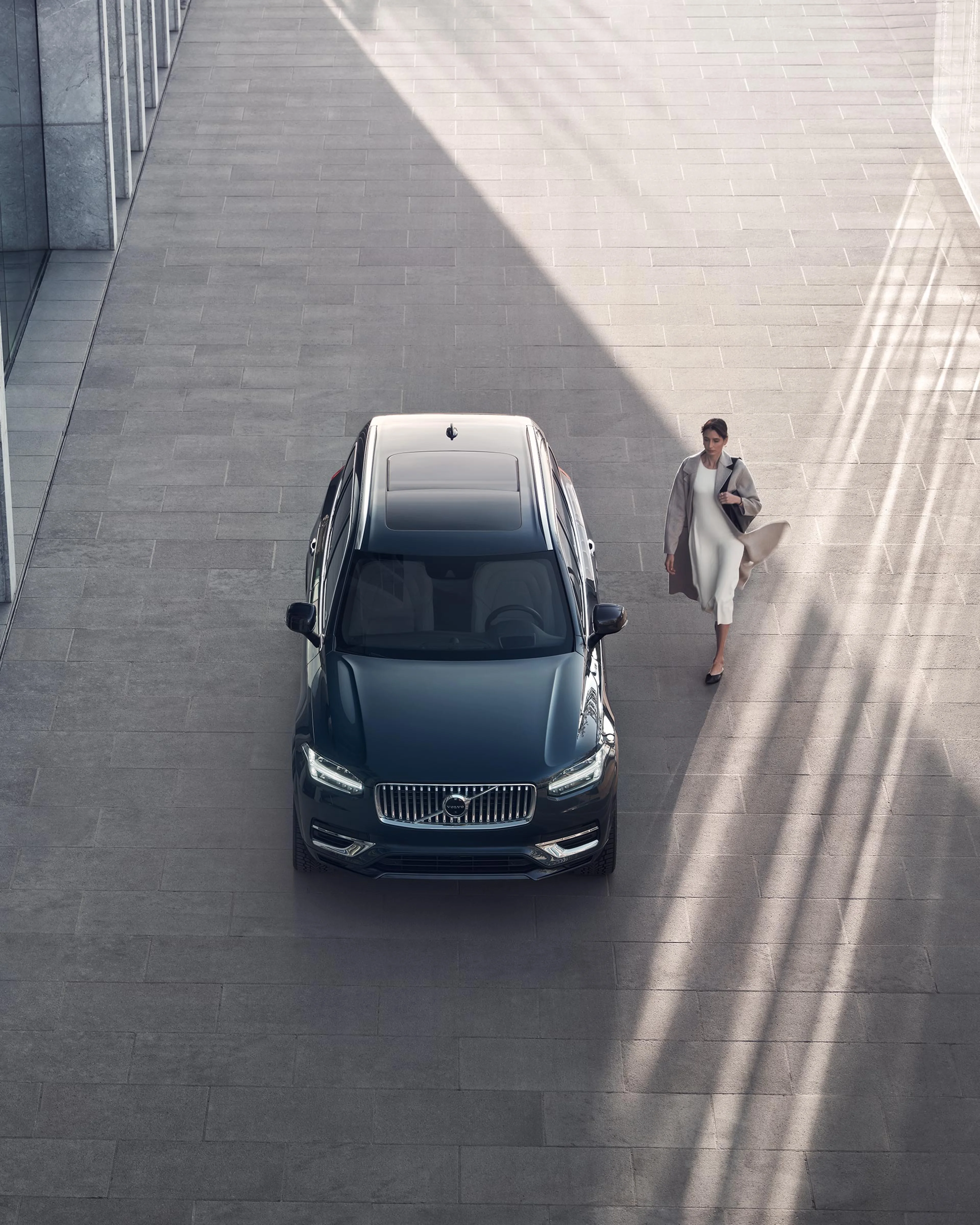 Eine Frau im Kleid geht auf einen dunkelgrauen XC90 zu.