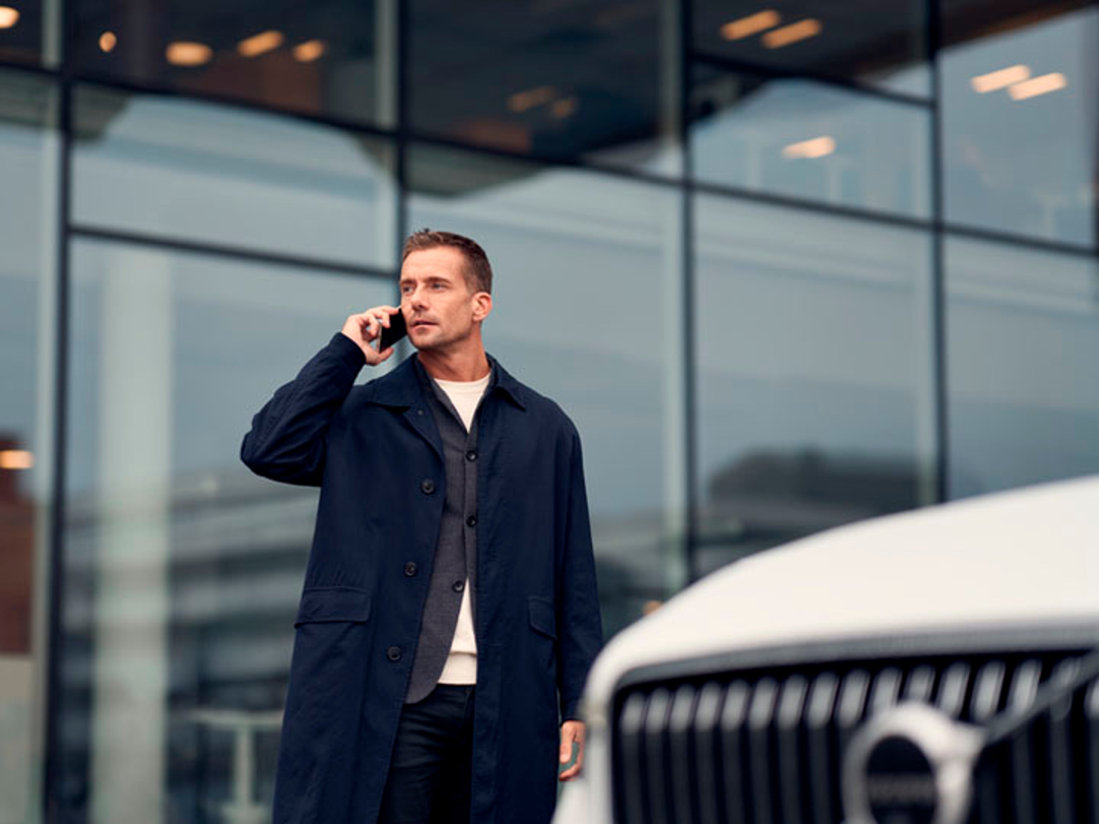 Un hombre hablando por un móvil con un Volvo delante