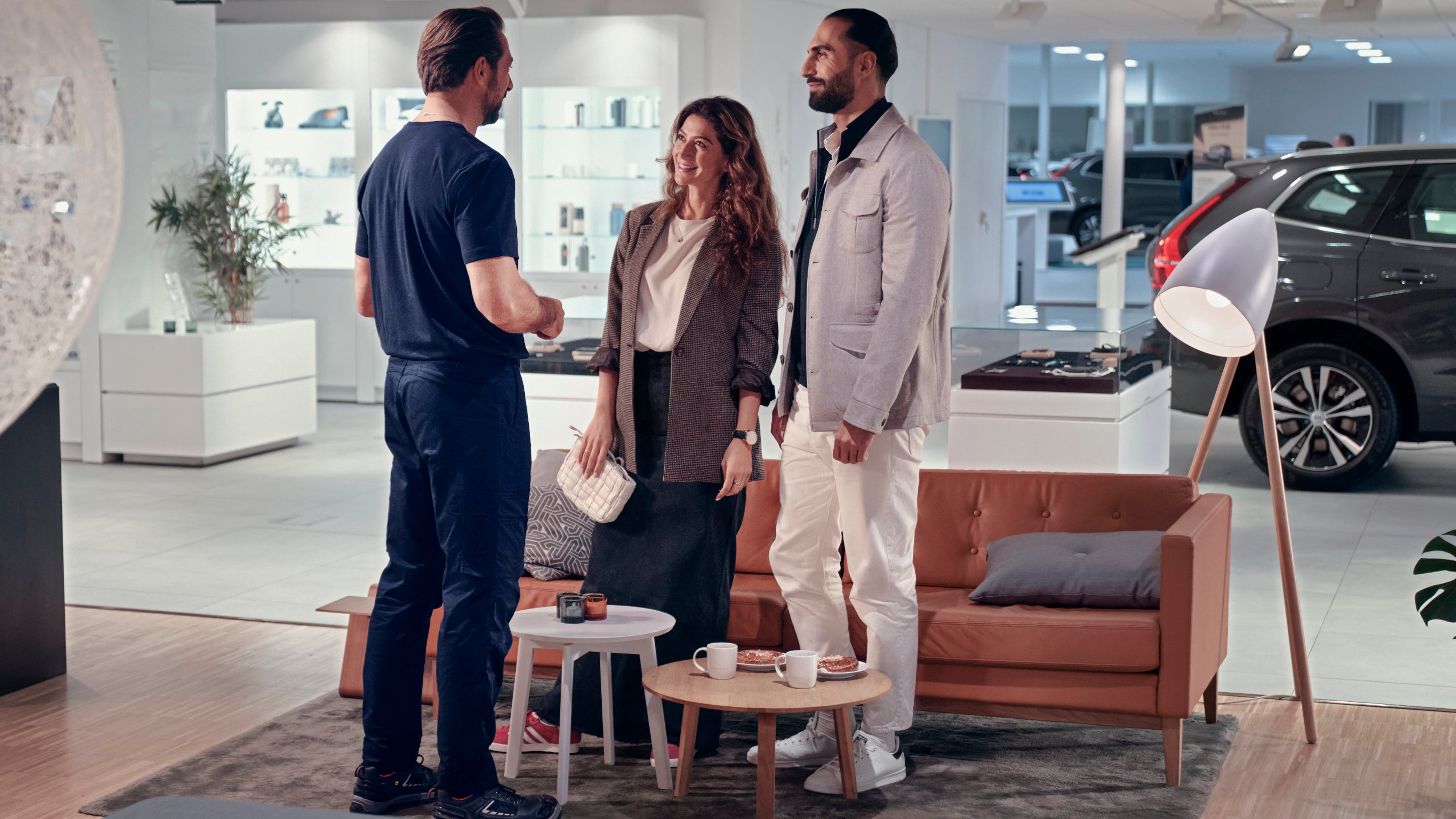 Zwei Personen stehen in einem Service und Beratungszimmer von einem Volvo Authohaus und werden von einem Sericetechniker beraten.