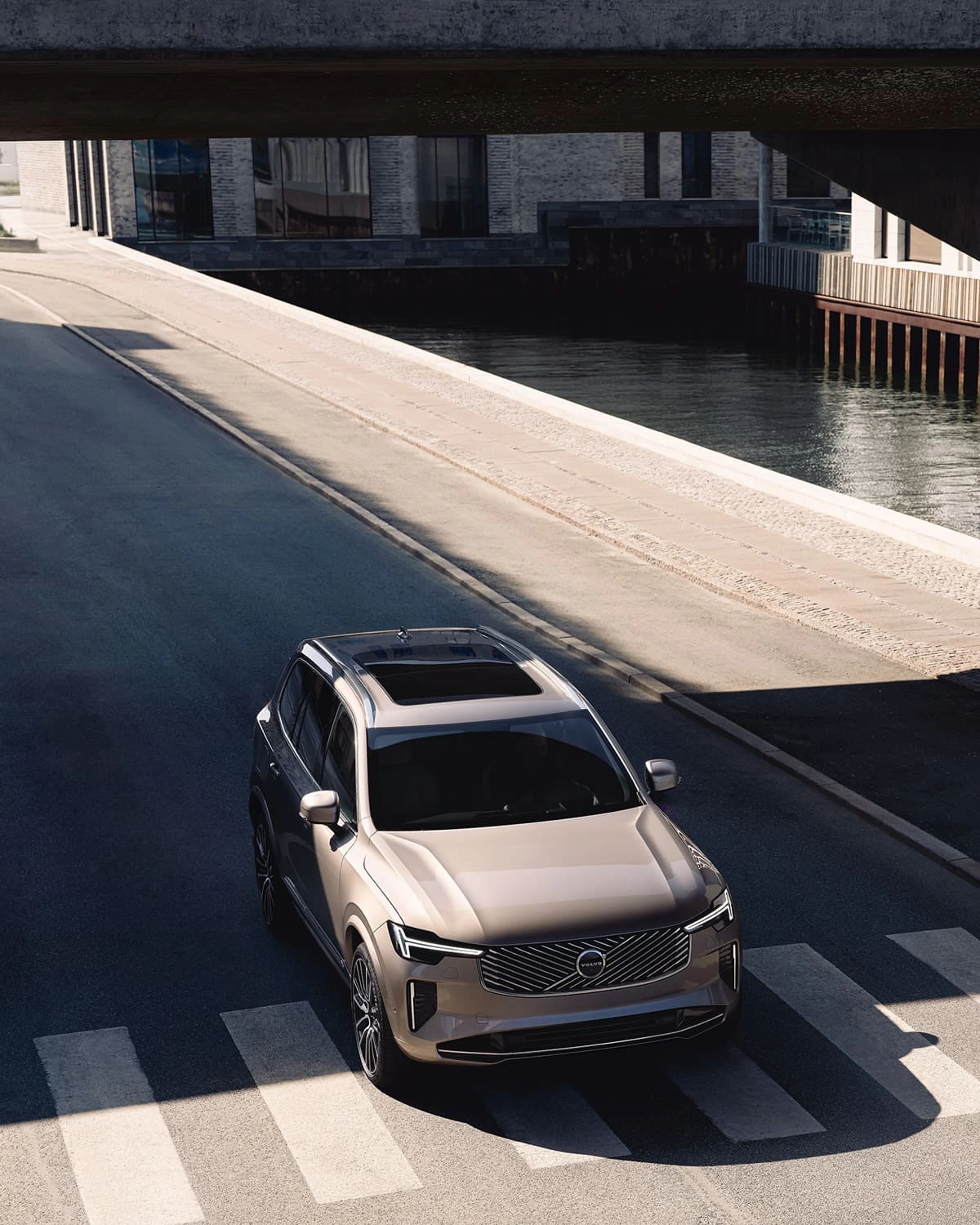 Une Volvo XC90 plug-in hybrid beige traverse un passage piéton en ville.
