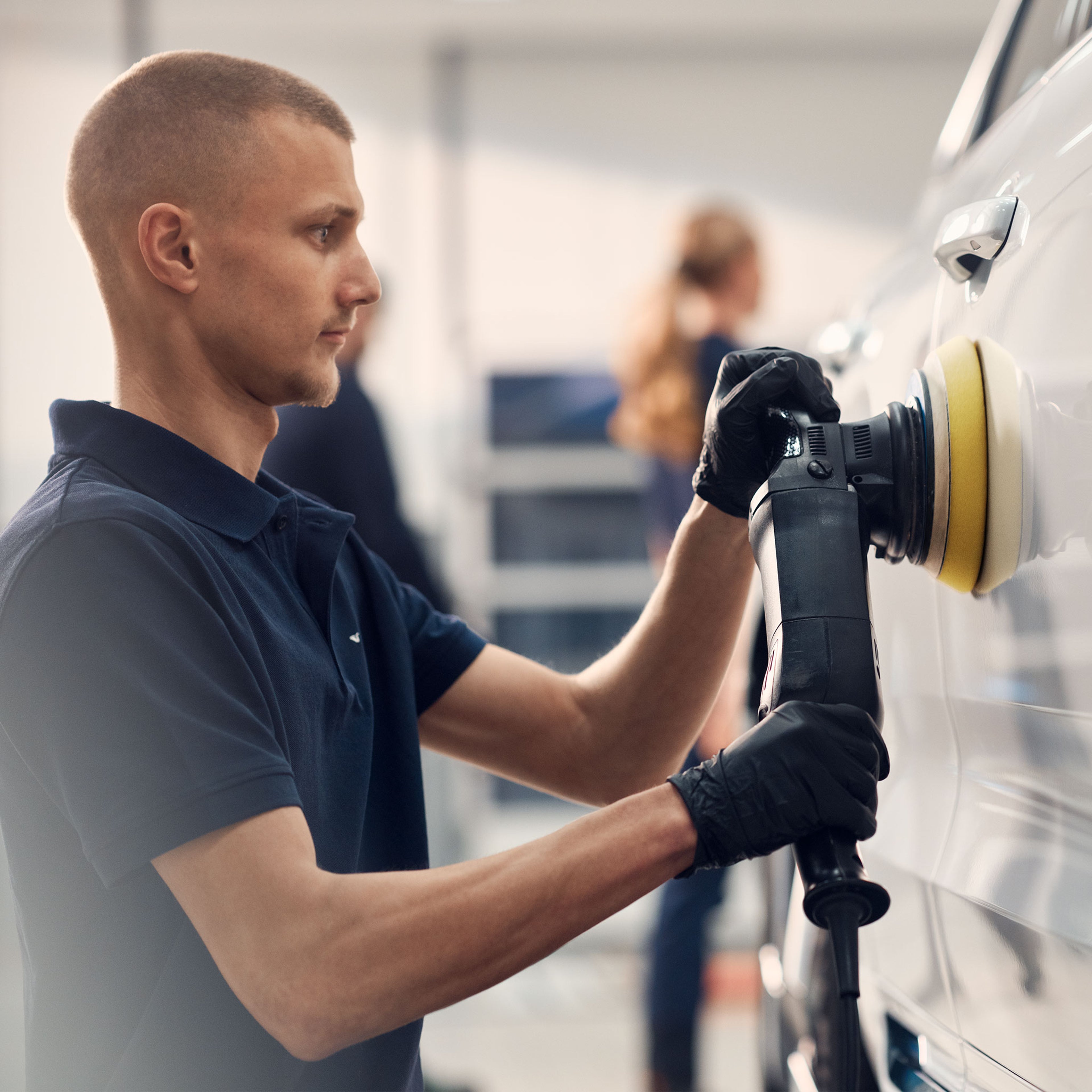 Volvo Omamekaanikko killoittaa kiilloituskoneella valkoisen Volvo -auton matkustajanpuoleisen etuoven maalipintaa.