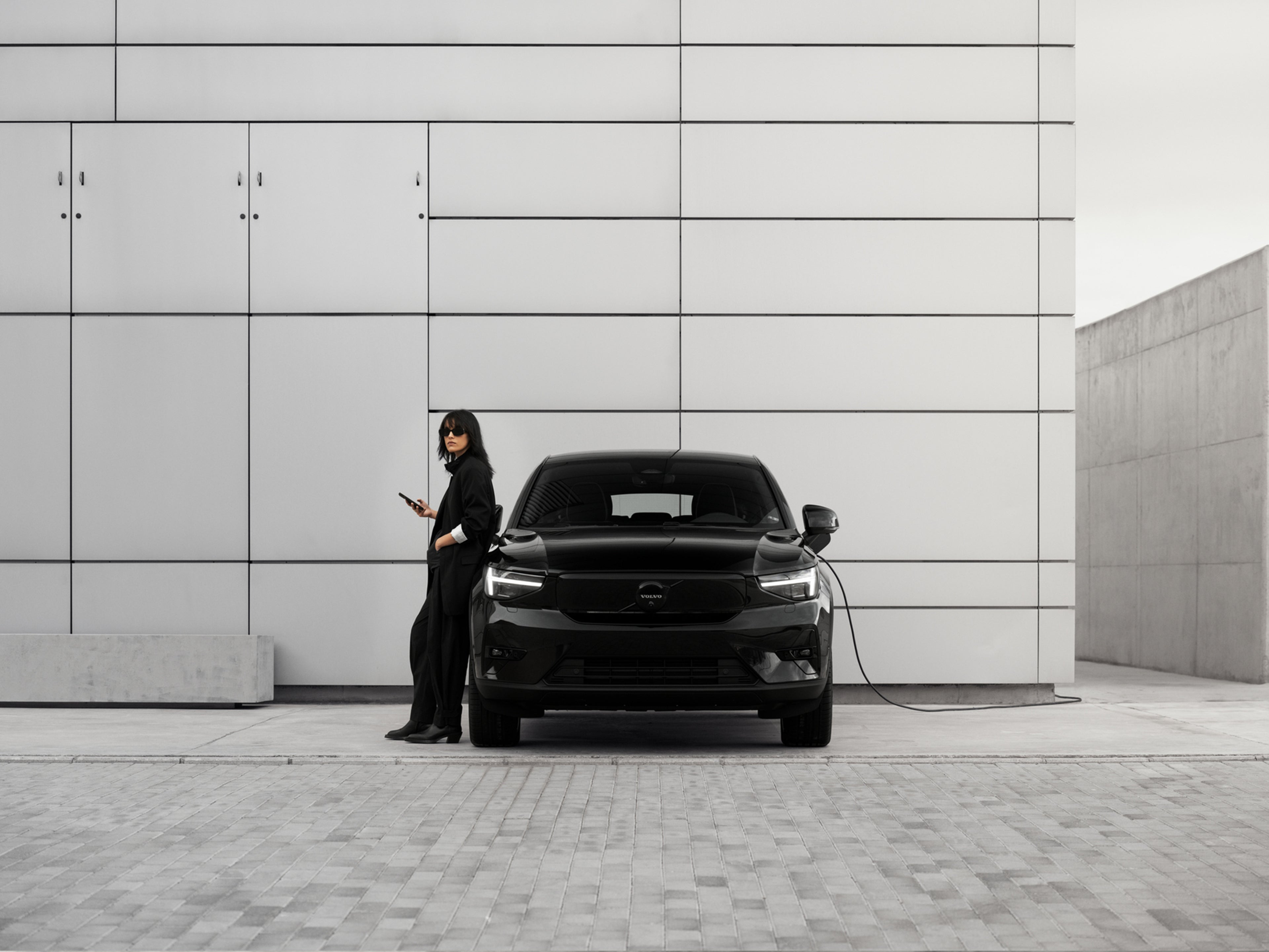 Nainen nojaa lataukseen kytkettyyn Volvo EC40 Black Edition autoon.