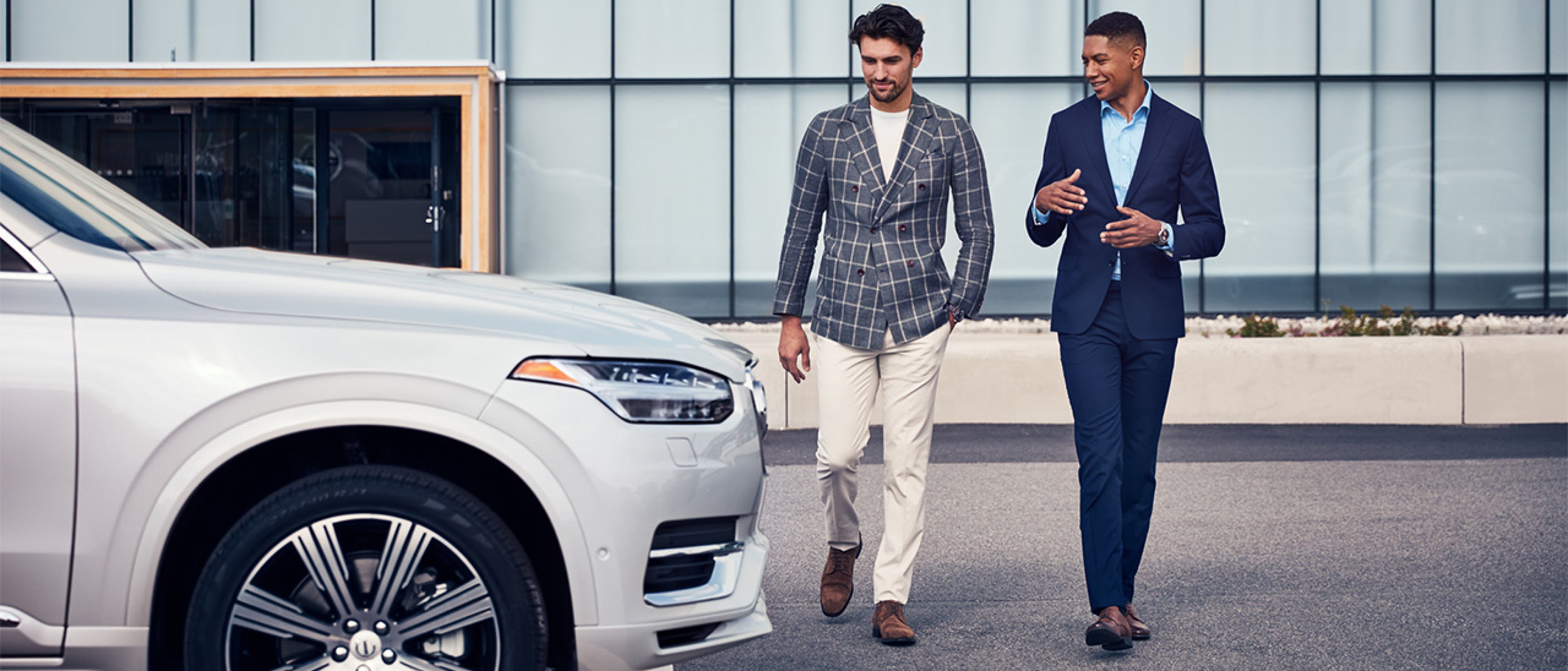 Two people in suit jackets walking and talking beside a Volvo car