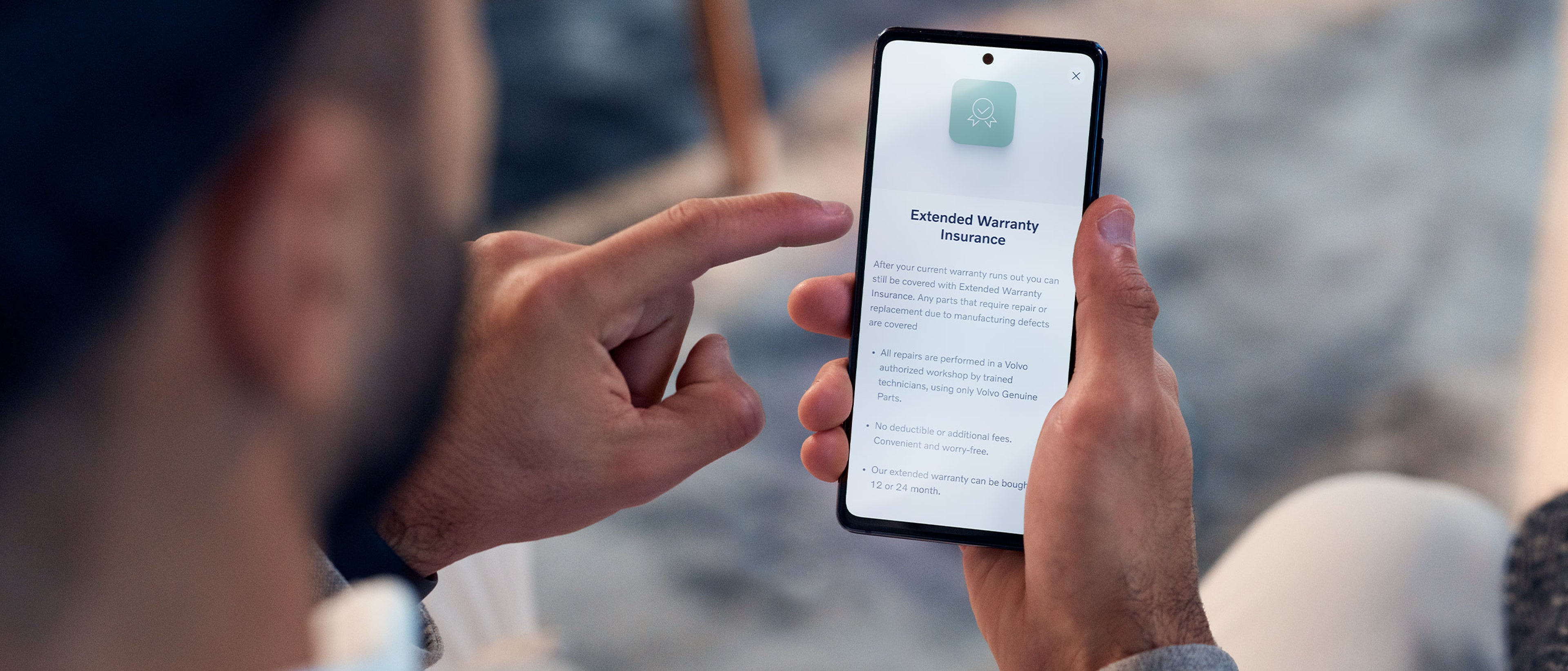 Ein Mann hält ein Handy in der Hand auf dessen Display "Extended Warranty Insurance" steht.