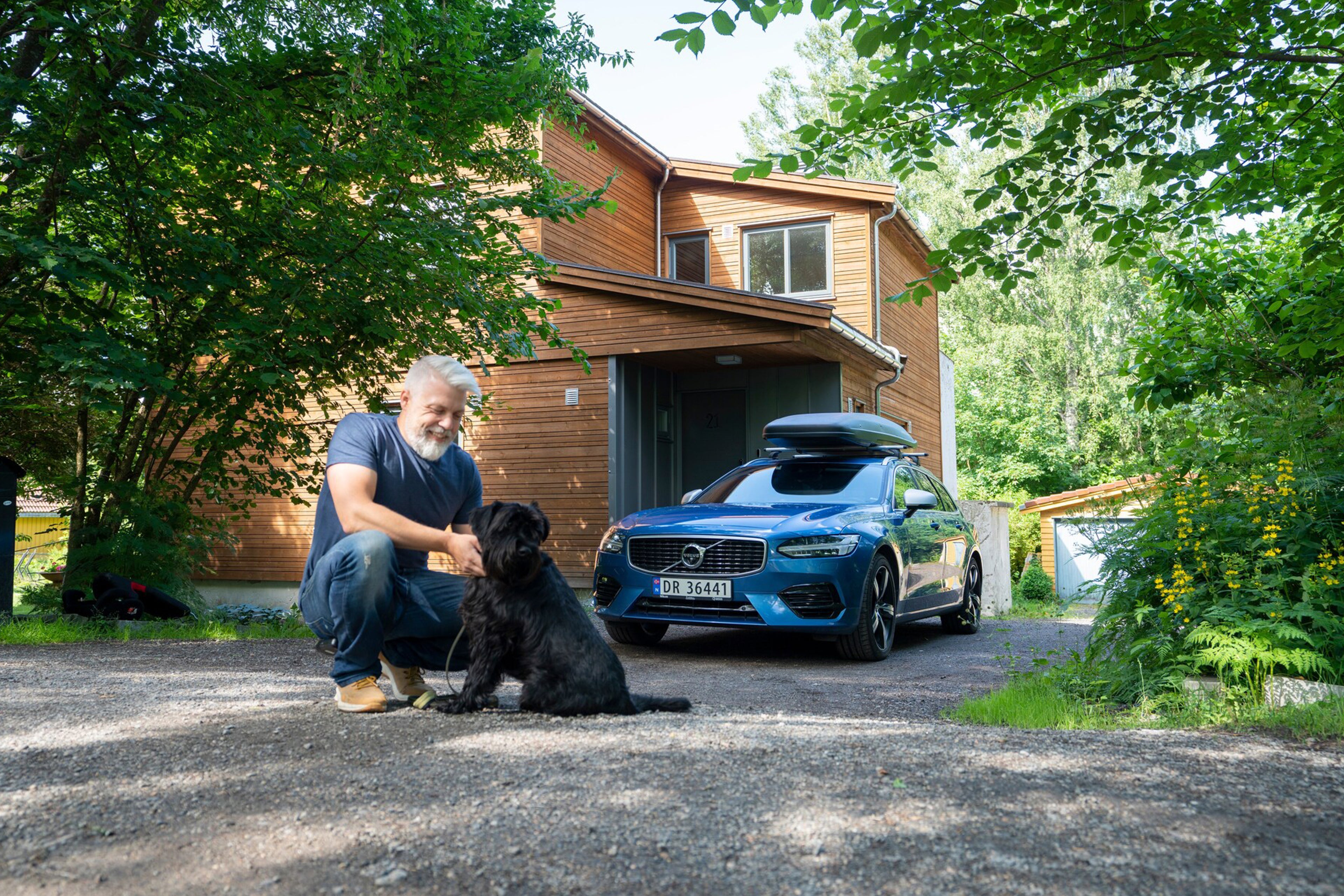 Mann med hunden sin står foran en blå Volvo