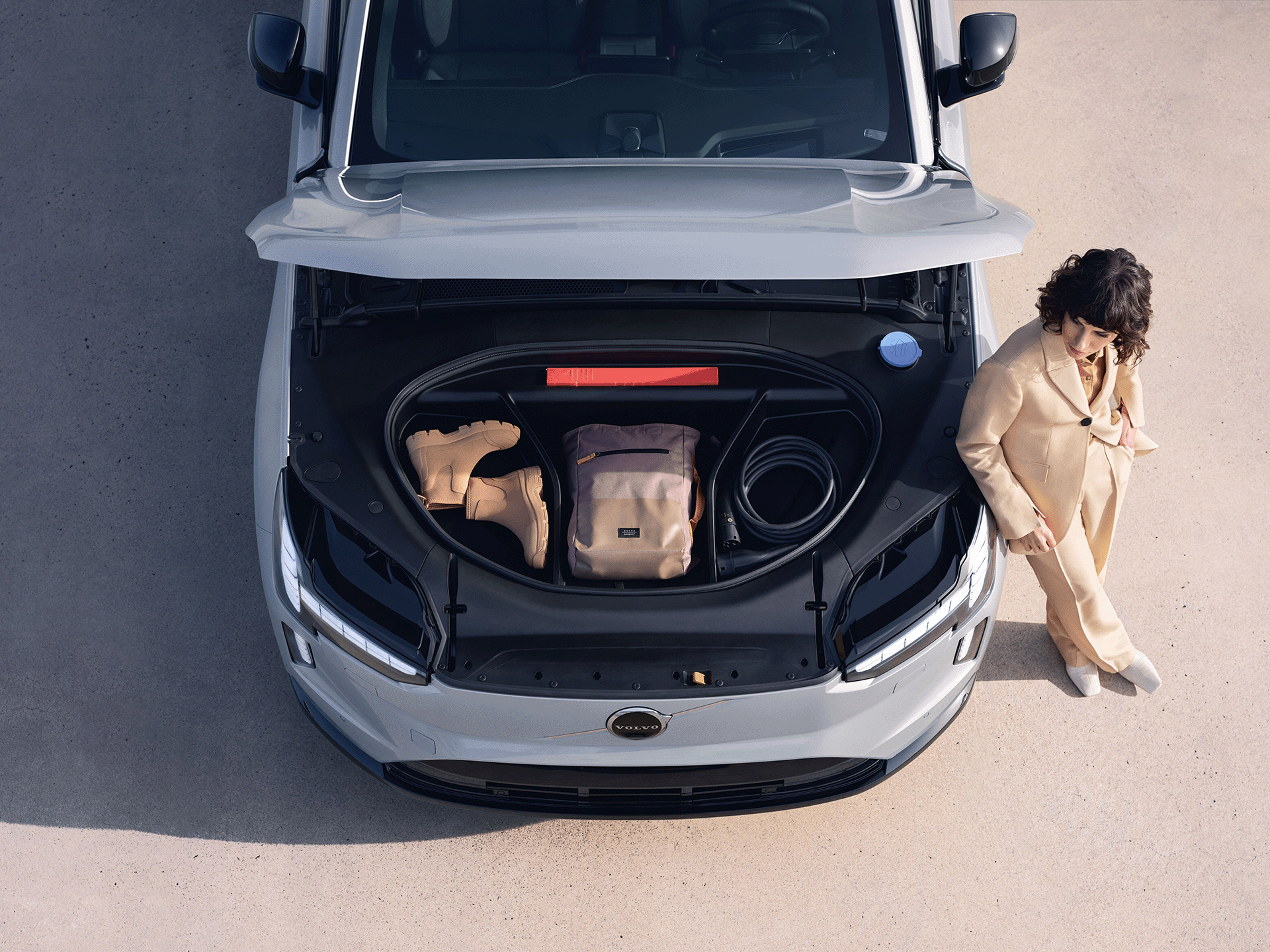 Eine Frau lehnt an einem Volvo EX90 mit geöffnetem Kofferraum.