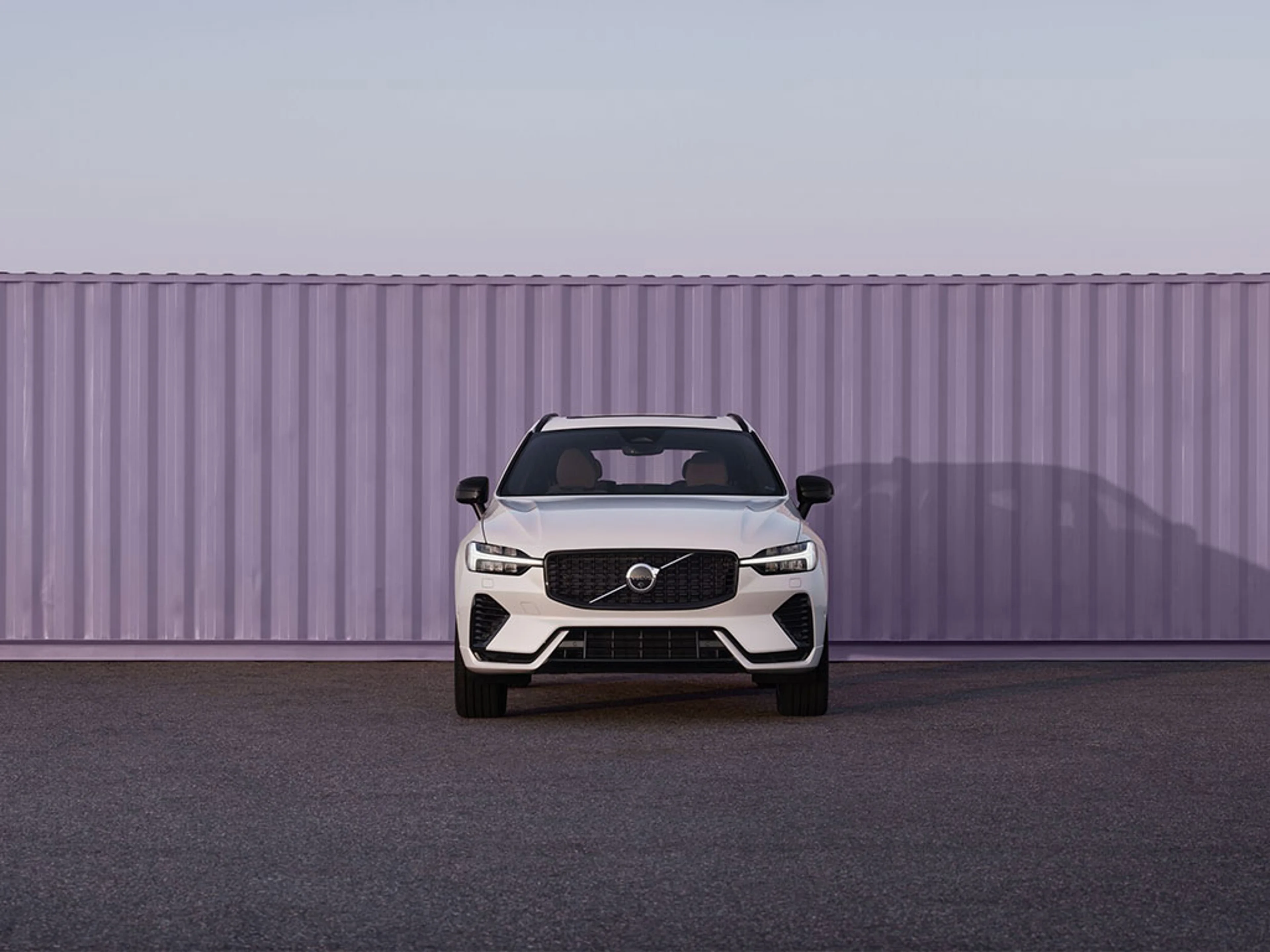 SUV Volvo blanc garé devant un grand conteneur violet sur une surface en asphalte.