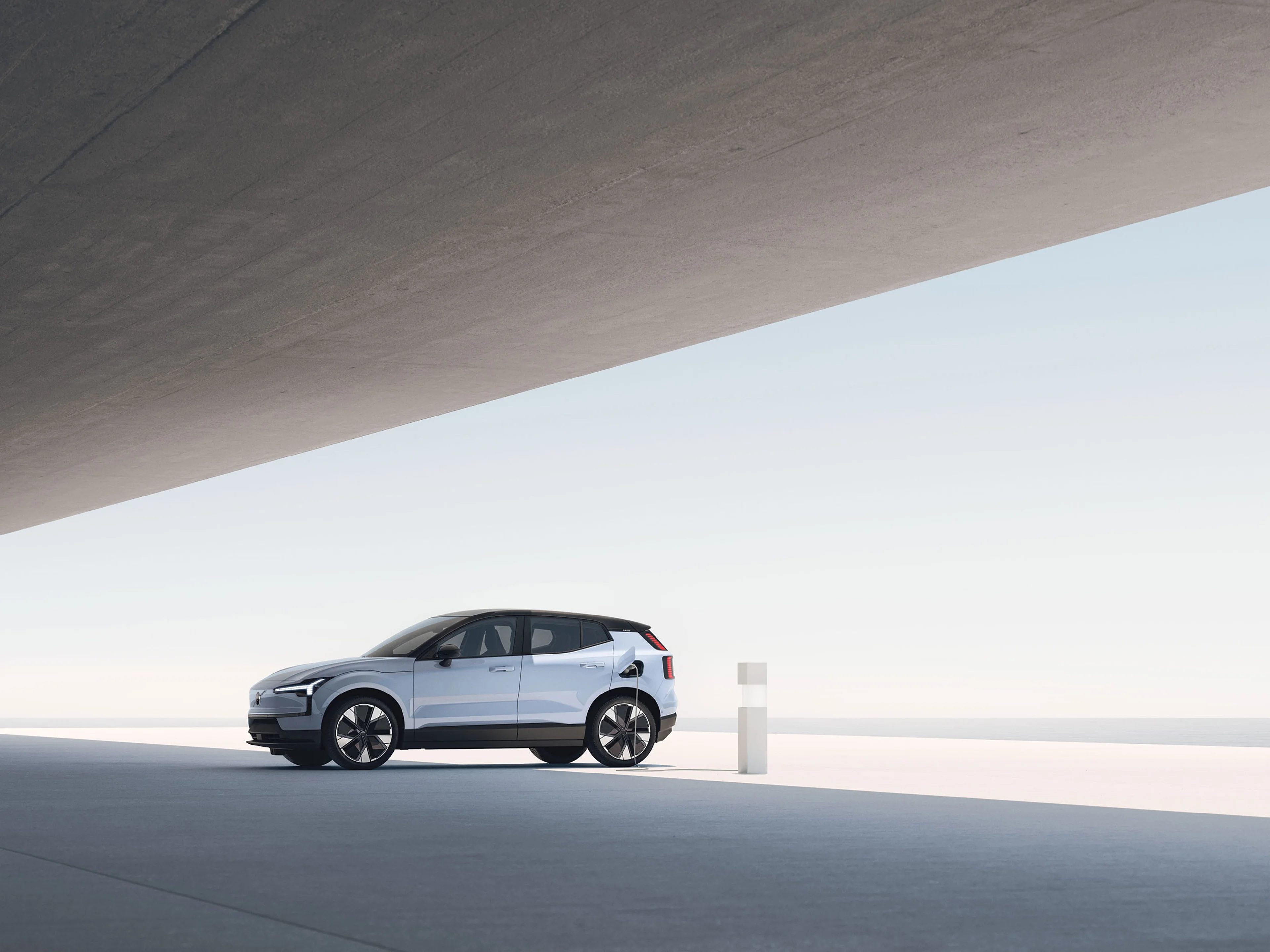 Vue latérale d’un Volvo EX30 blanc moderne avec toit noir et grandes roues, dans un décor minimaliste