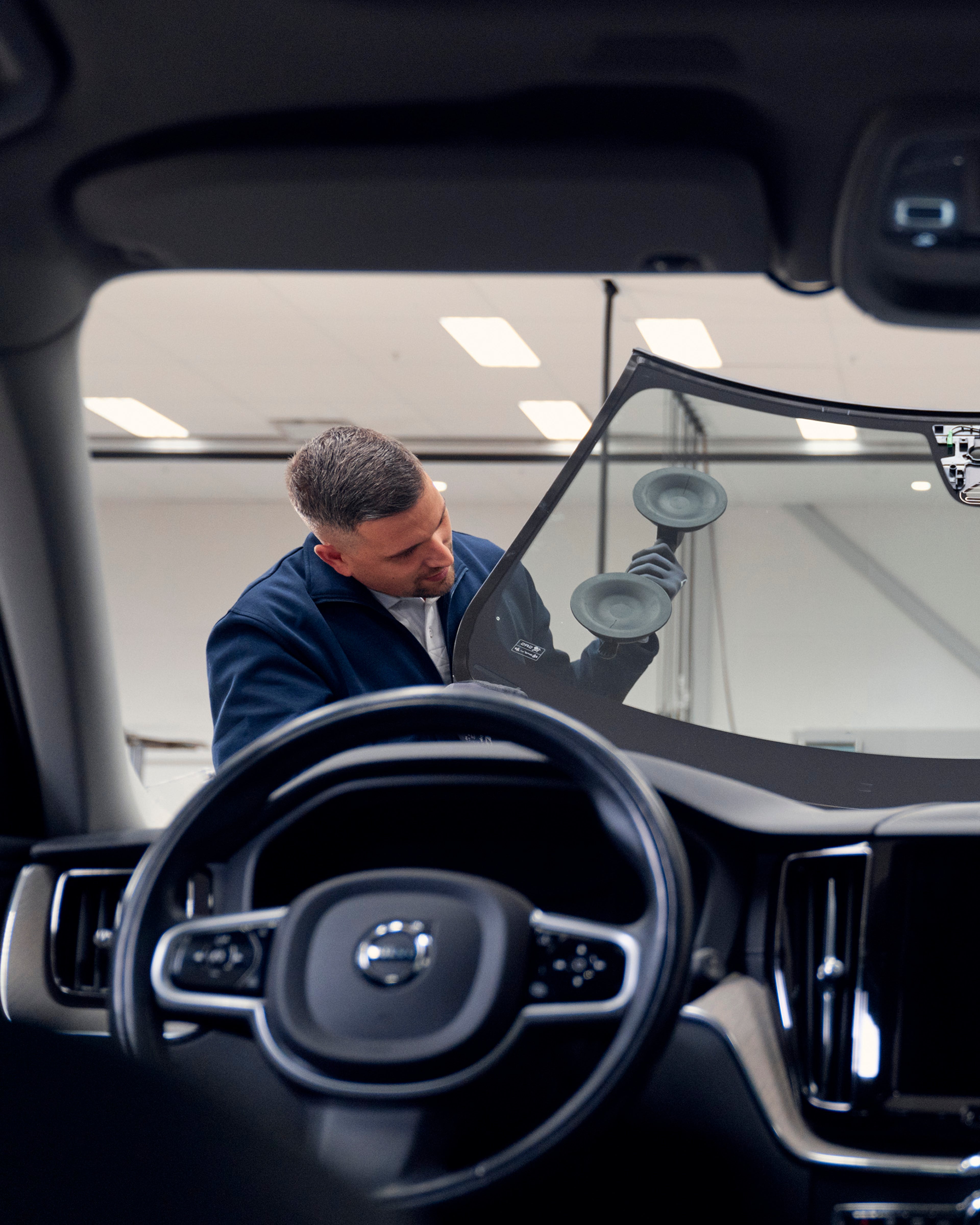 Dos mecánicos manipulando un parabrisas de un vehículo Volvo