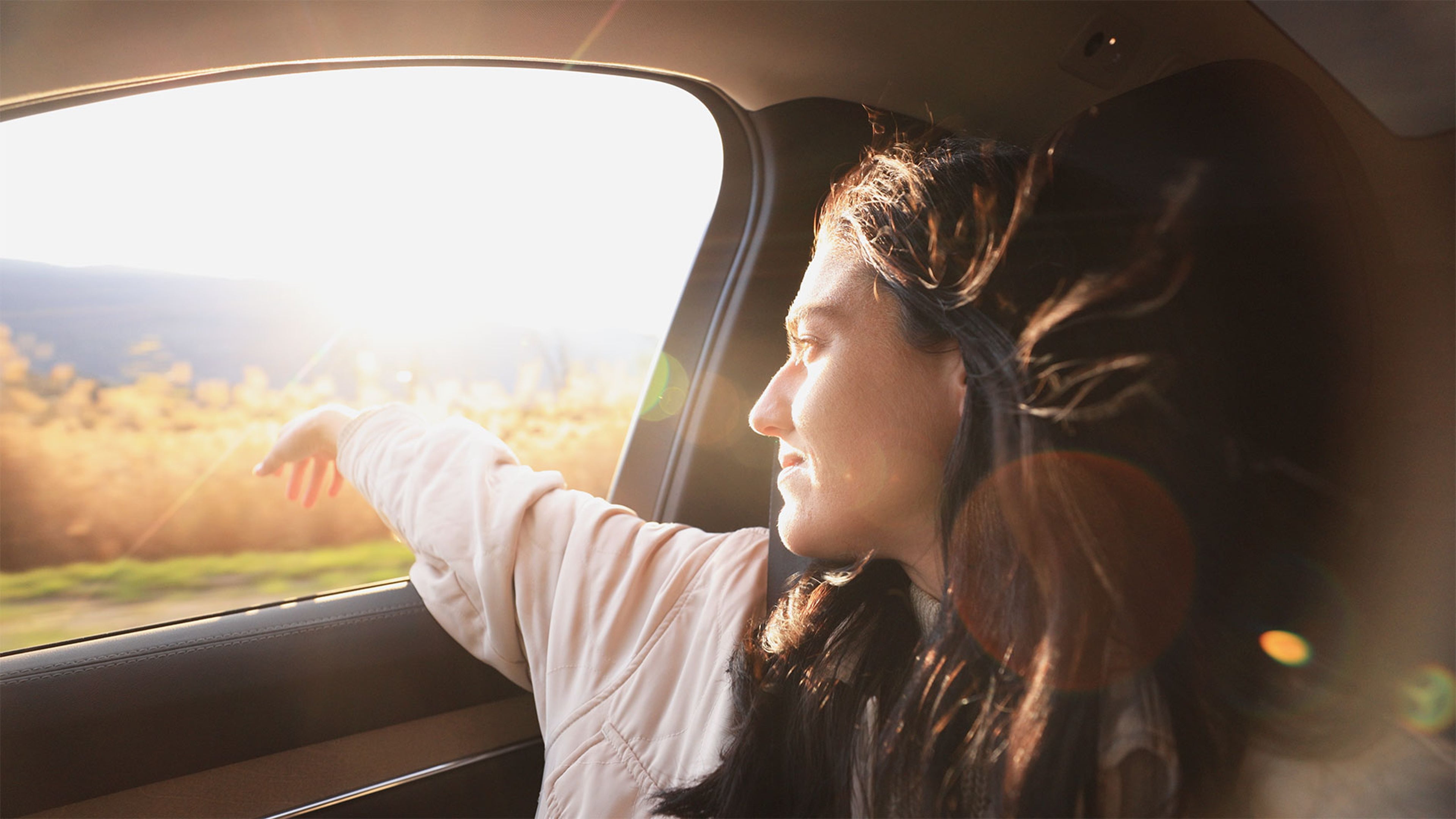 Personne assise en voiture, bras sur la fenêtre ouverte, regardant un paysage ensoleillé.
