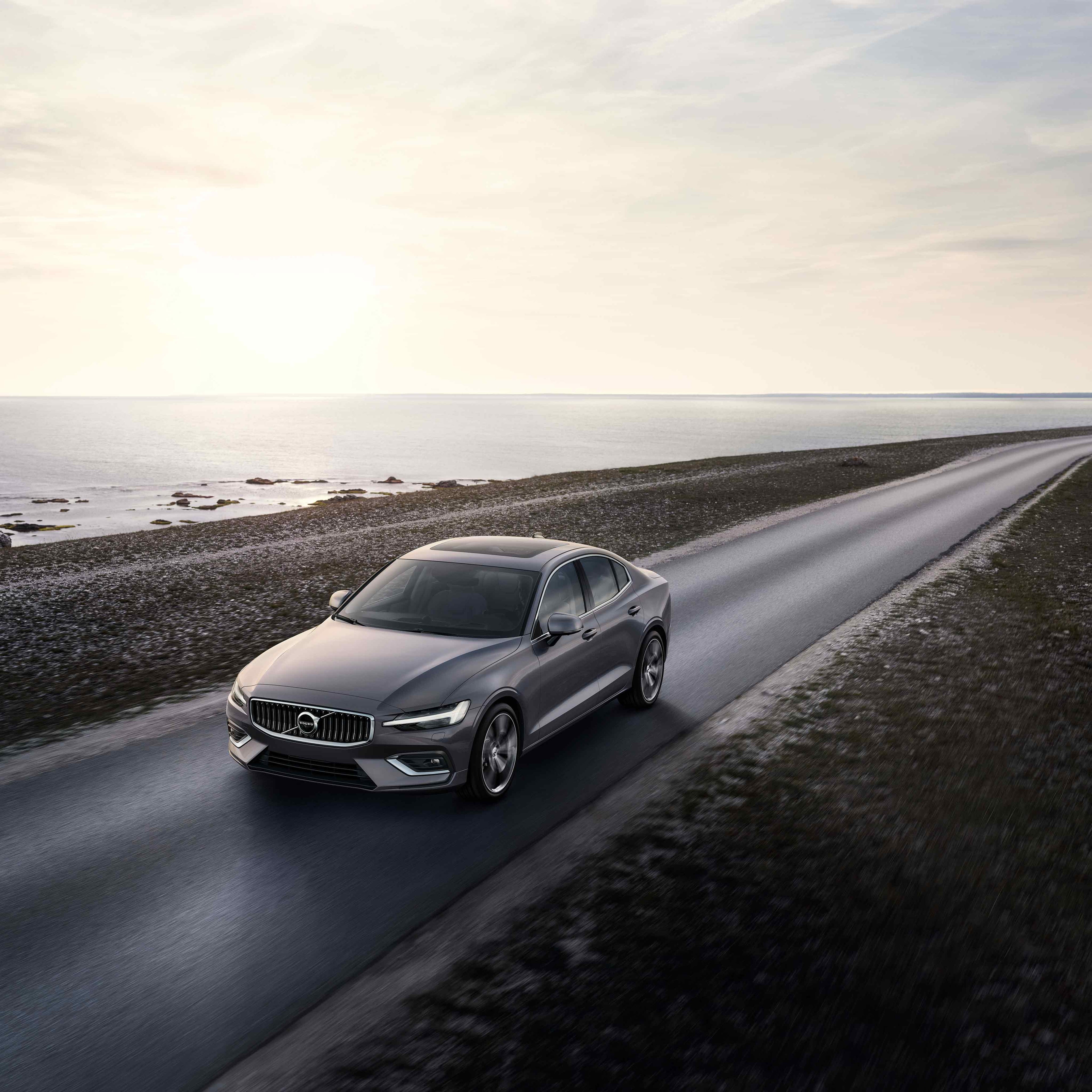 Metallinharmaa Volco S60 ajaa auringonlaskussa rantatietä.