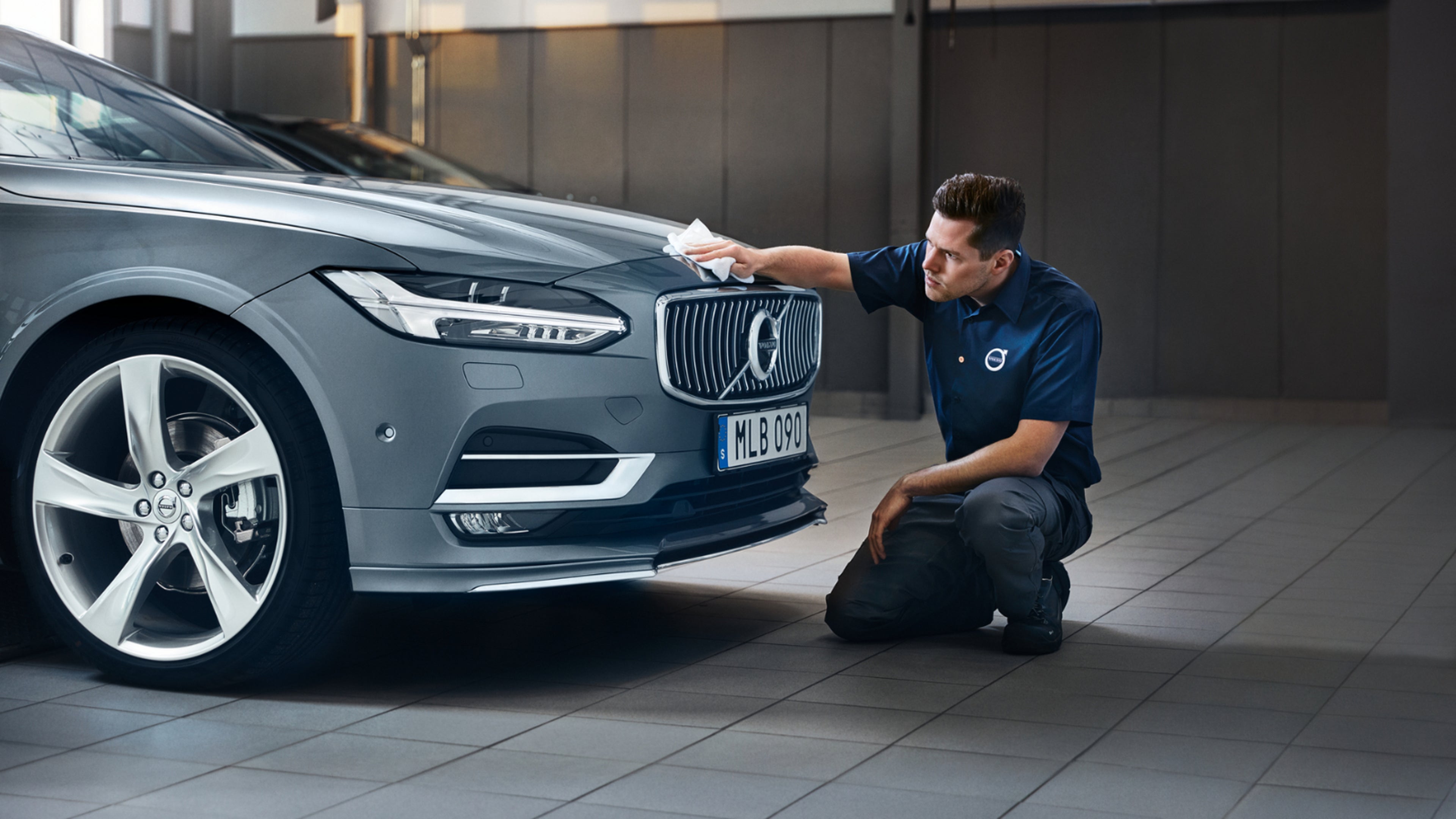 Ein Volvo Mitarbeiter reinigt mit einem Tuch den vorderen Teil eine Volvo Fahrzeugs.