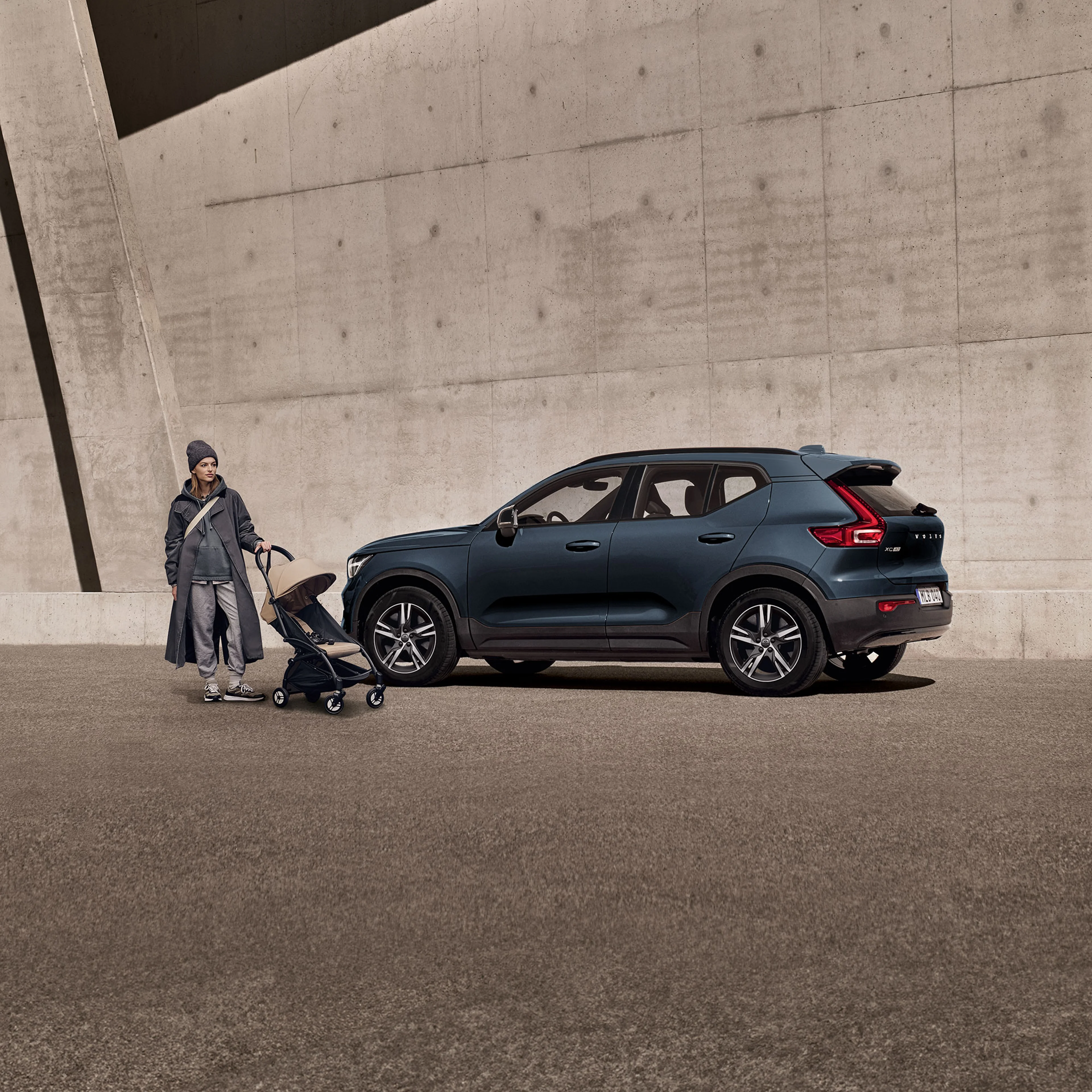 Personne poussant une poussette près d’une Volvo XC40 bleue garée devant un mur en béton