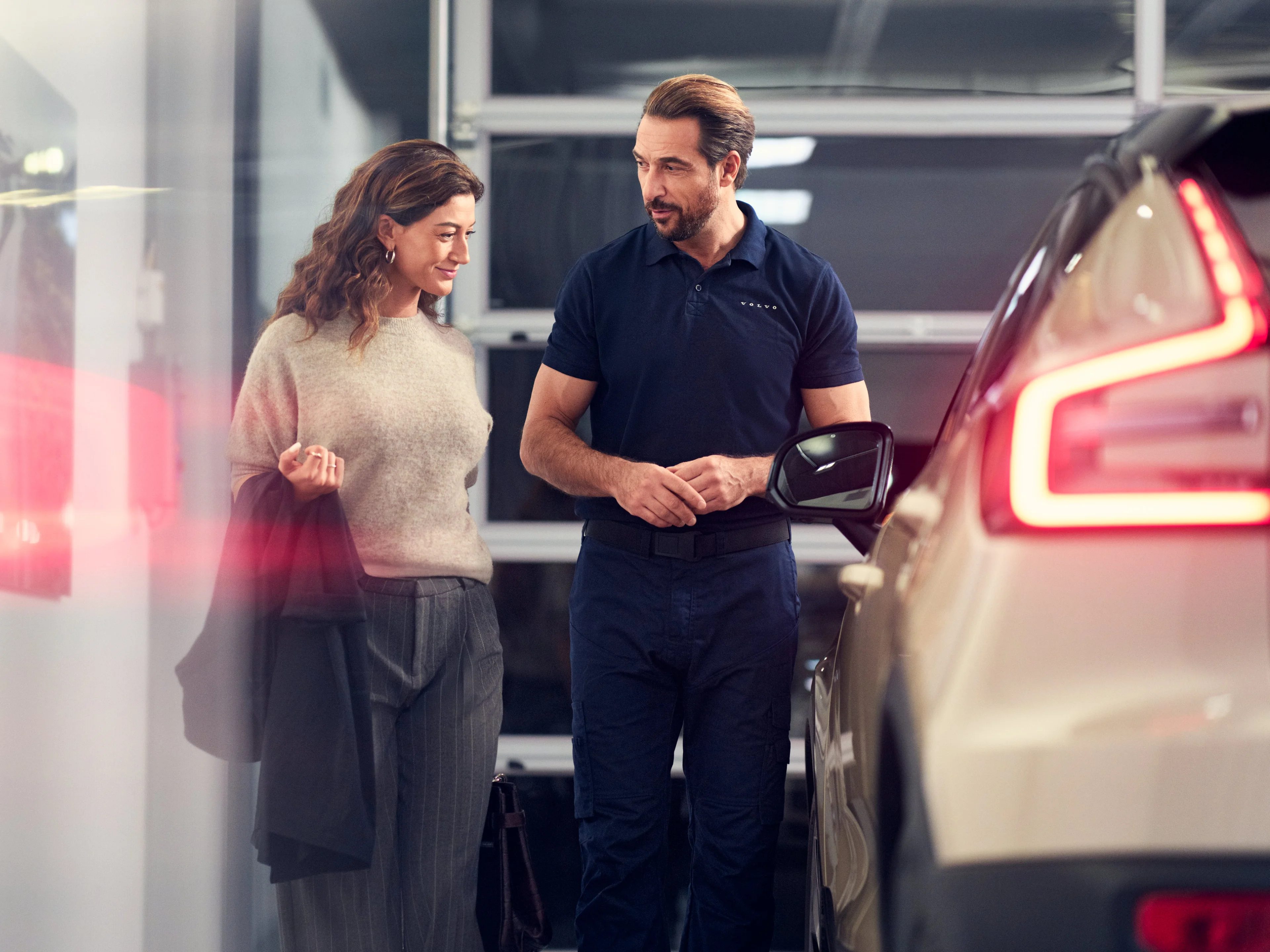 Eine Frau und ein Volvo Servicetechniker stehen neben einem beigen Volvo Fahrzeug uterhalten sich und schauen es an.