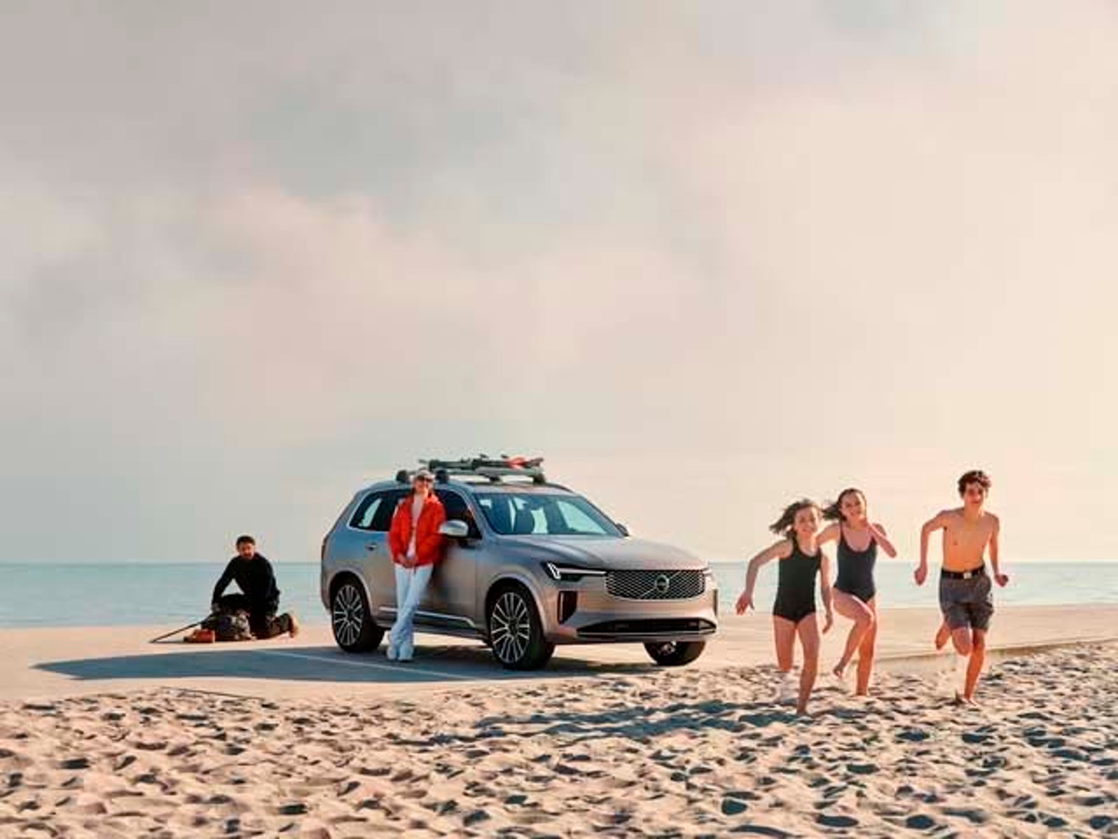 Un Volvo SUV en la playa con accesorios en el techo y unos chicos corriendo