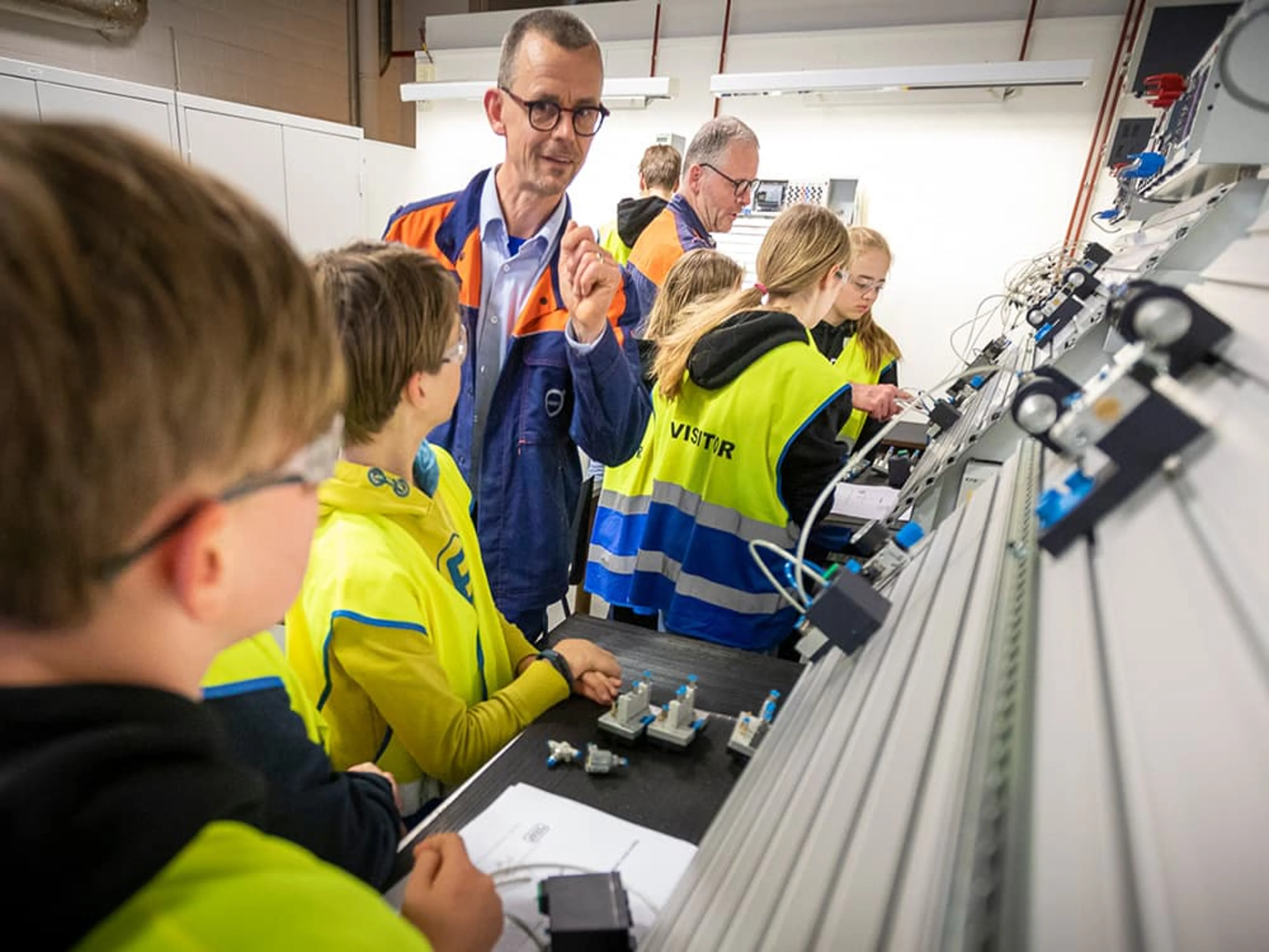 Un groupe d'enfants portant des gilets de sécurité jaunes reçoivent des explications d'un employé de Volvo sur un appareil technique.
