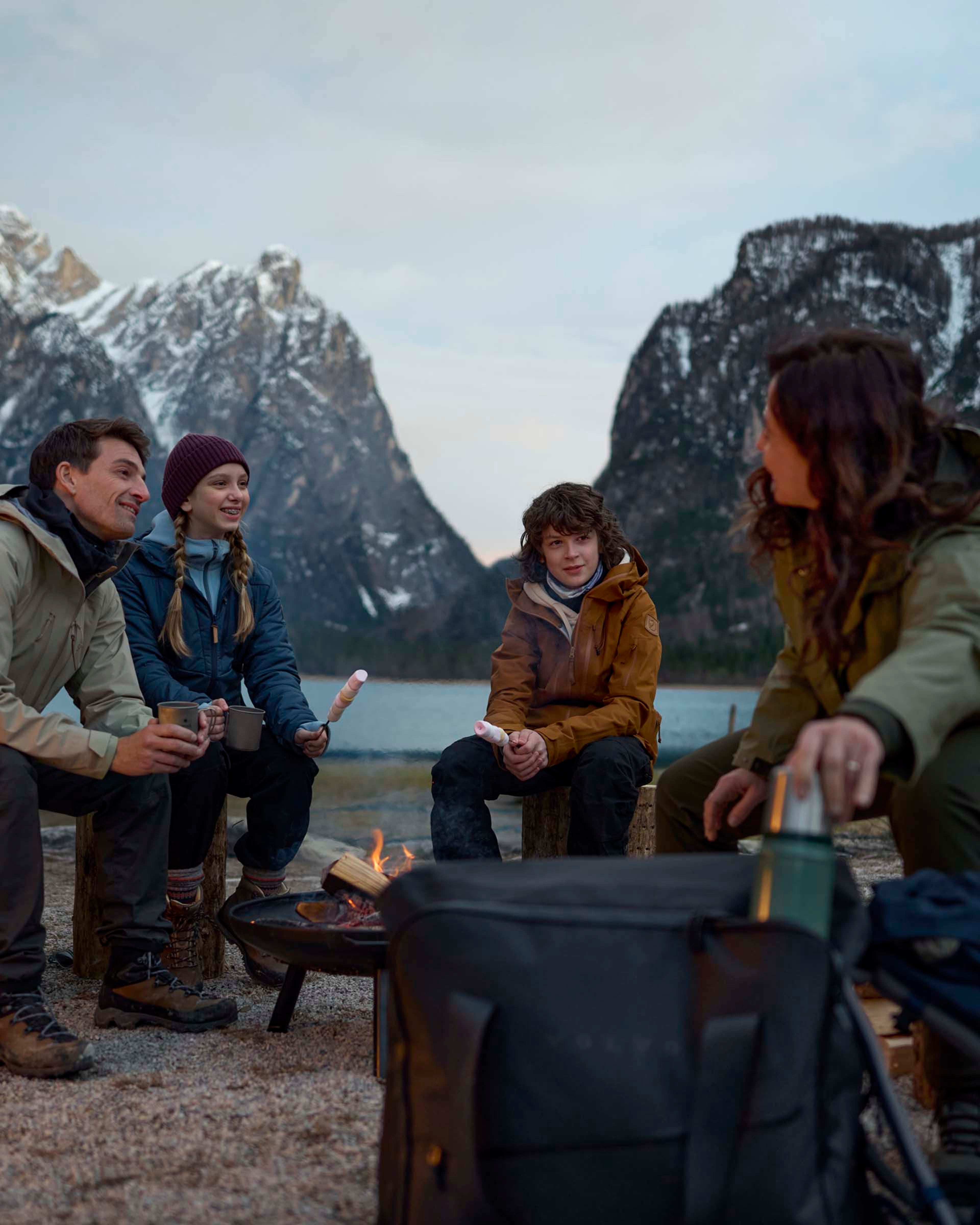 Un grupo de personas conversando rodeados entre montañas nevadas y un lago a sus espaldas