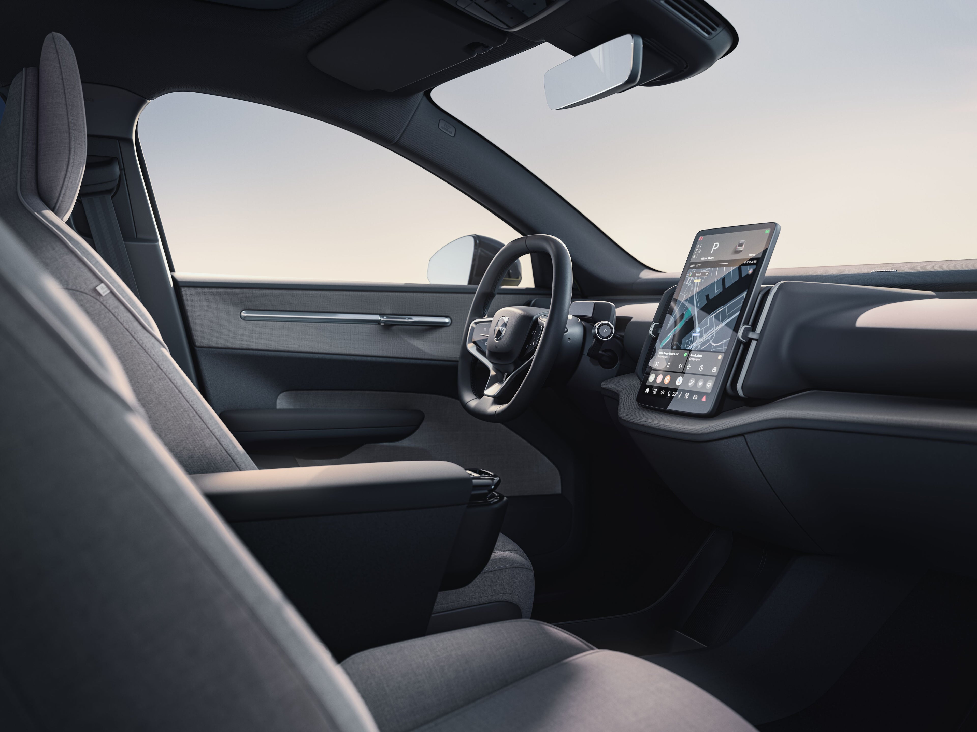 Intérieur d’une voiture Volvo électrique avec écran tactile central, volant et sièges avant en tissu gris.